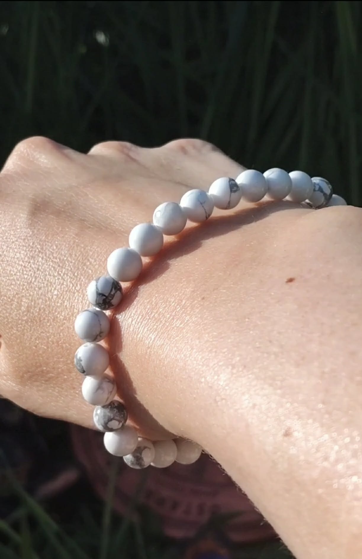Bracelet howlite blanche 6 mm porté au poignet sur fond sombre, perles blanches veinées de gris pour calme du cœur, retenue émotionnelle et sérénité