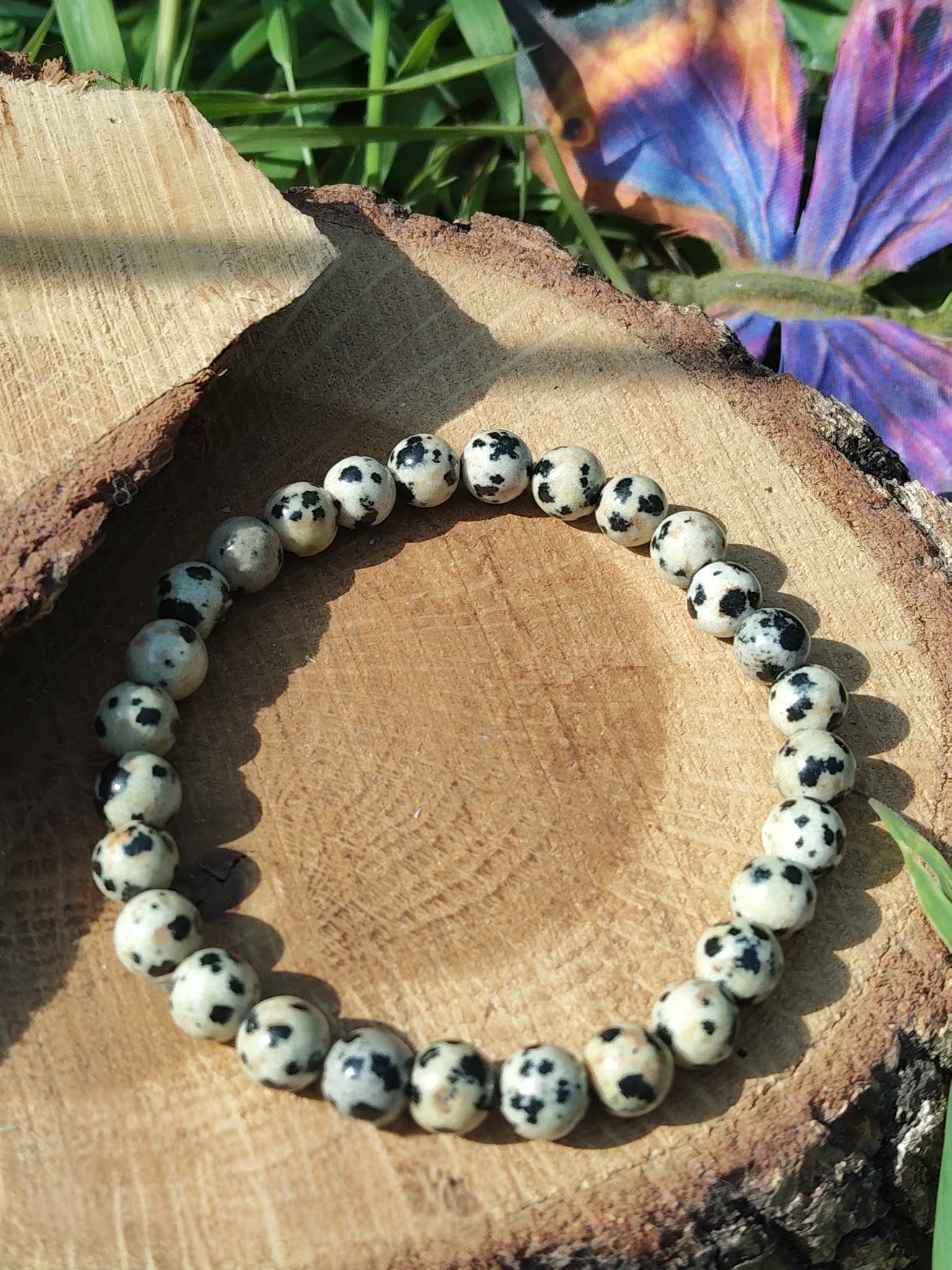 Bracelet jaspe dalmatien 6 mm sur bois avec fleur violette en arrière-plan, perles ivoire mouchetées de noir pour discernement et calme protecteur