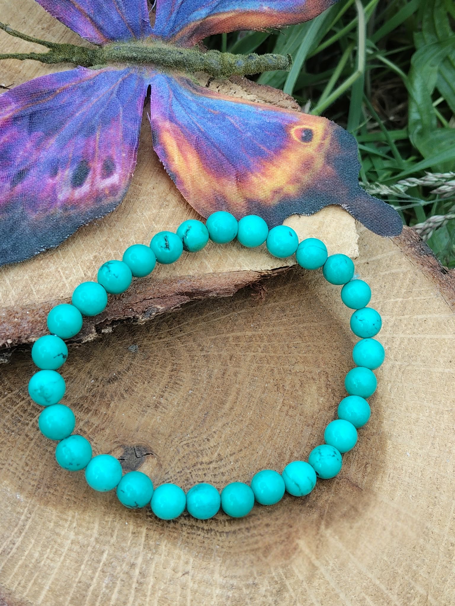 bracelet turquoise stabilisée perles rondes posé sur rondin de bois avec papillon violet protection en voyage et bouclier énergétique