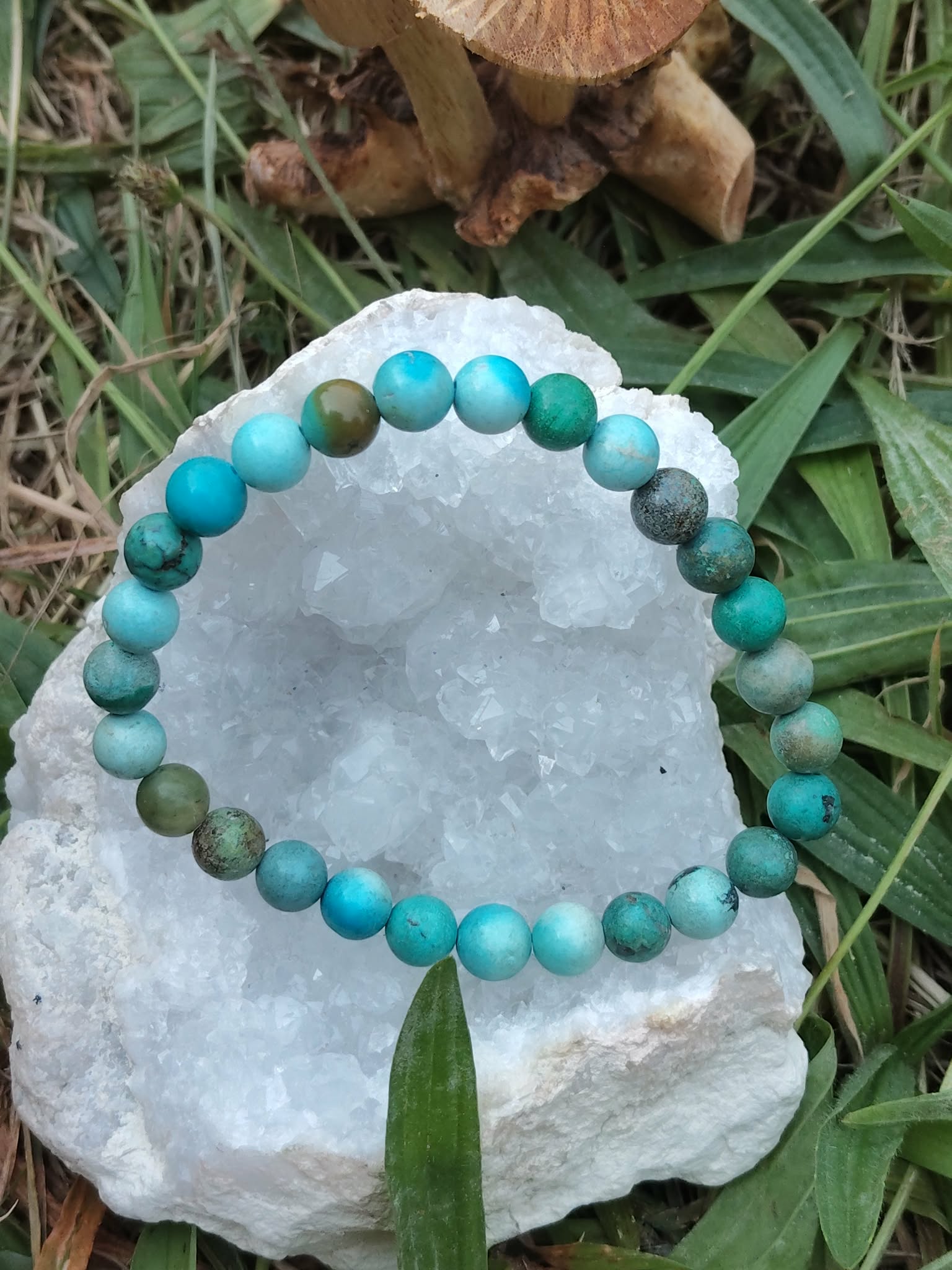 Bracelet turquoise du Tibet présenté sur un amas de quartz cristallisée avec herbes et champignons, équilibre émotionnel et protection douce