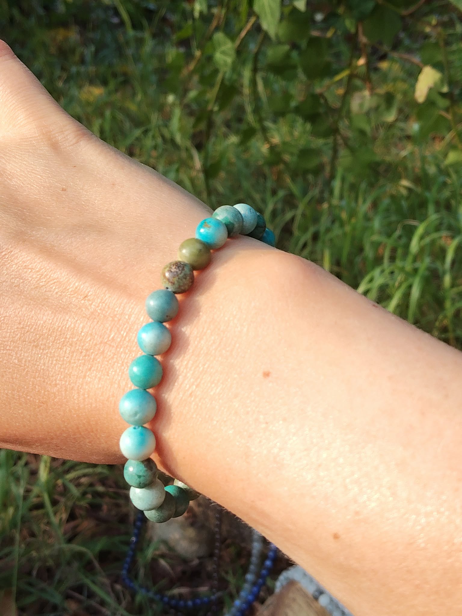 Bracelet turquoise du Tibet porté au poignet avec fond feuillage, pierre naturelle liée au calme mental et à l’expression apaisée