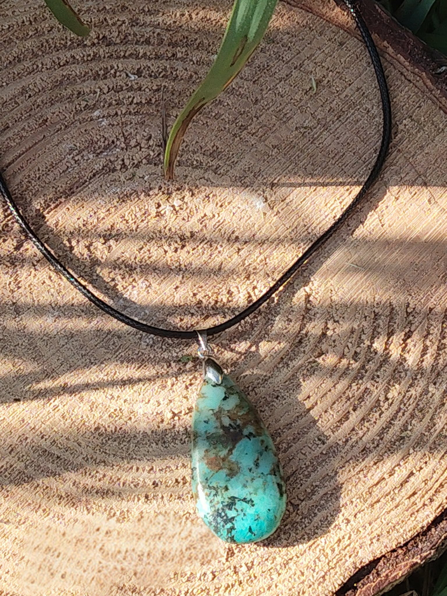Collier sur cordon noir avec pendentif turquoise africaine goutte bleu-vert posé sur rondelle de bois en décor nature, jaspe africain relié à l’ancrage doux, à la stabilité et à l’expression sincère.