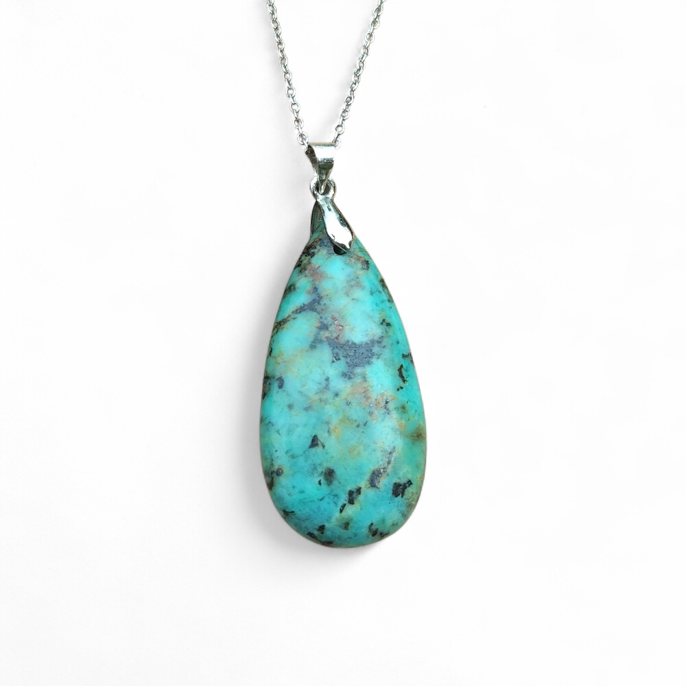 Pendentif turquoise africaine goutte bleu-vert sur bélière argentée, jaspe africain posé sur fond blanc, pierre naturelle reliée à la sérénité, à la parole fluide et à la confiance douce.