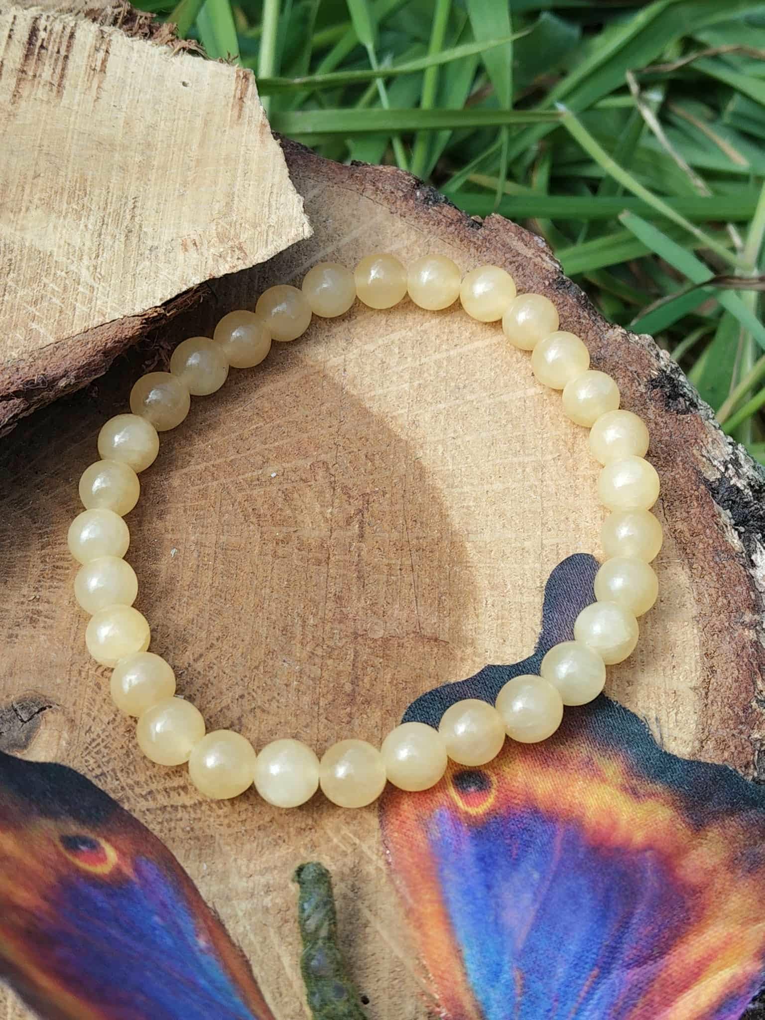 Bracelet calcite jaune sur rondin de bois avec feuillage vert et papillon, pierre naturelle liée à la concentration et au moral