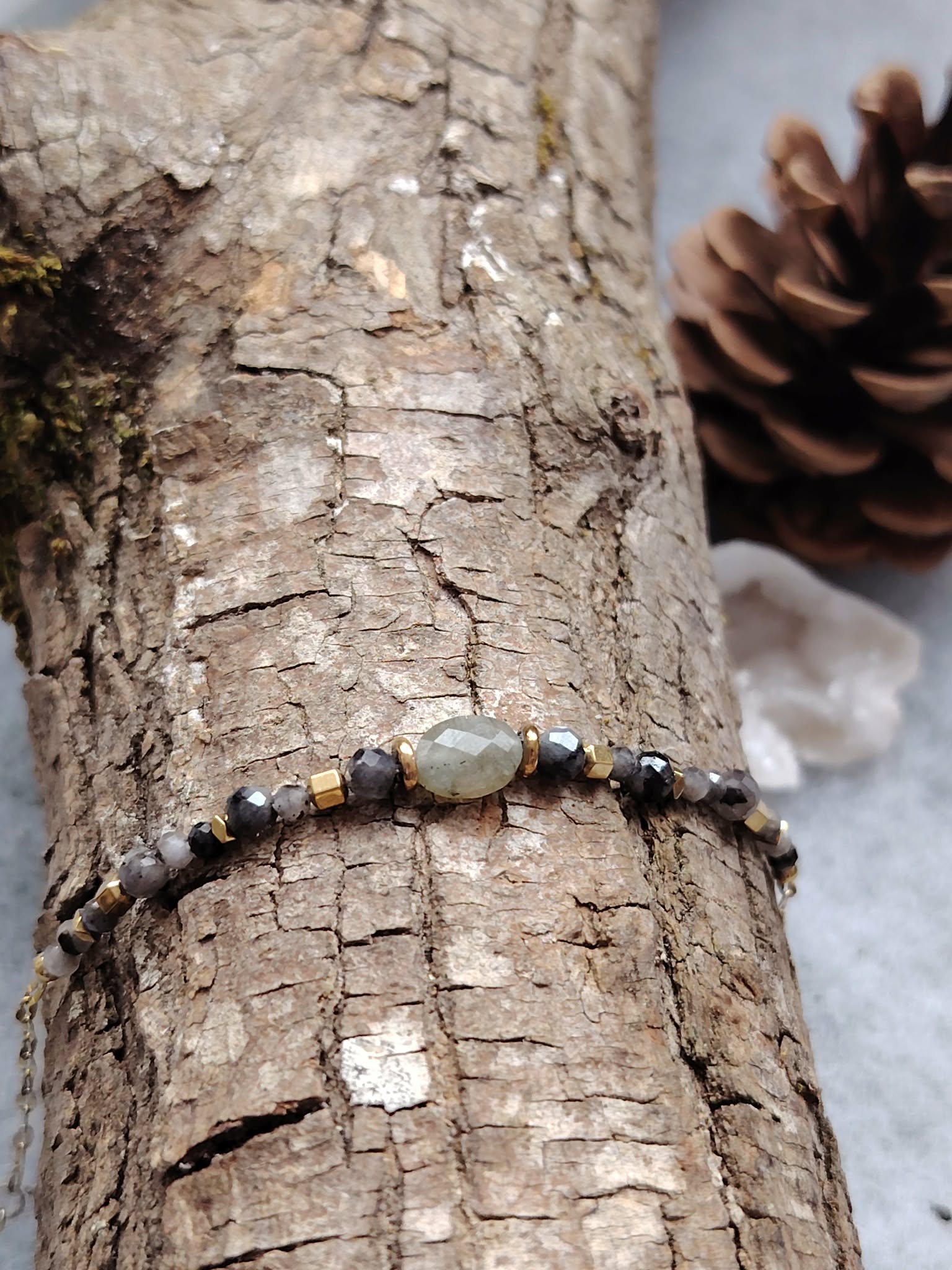 Bracelet en labradorite sur écorce avec pomme de pin, décor nature boisé, enracinement paisible et sérénité