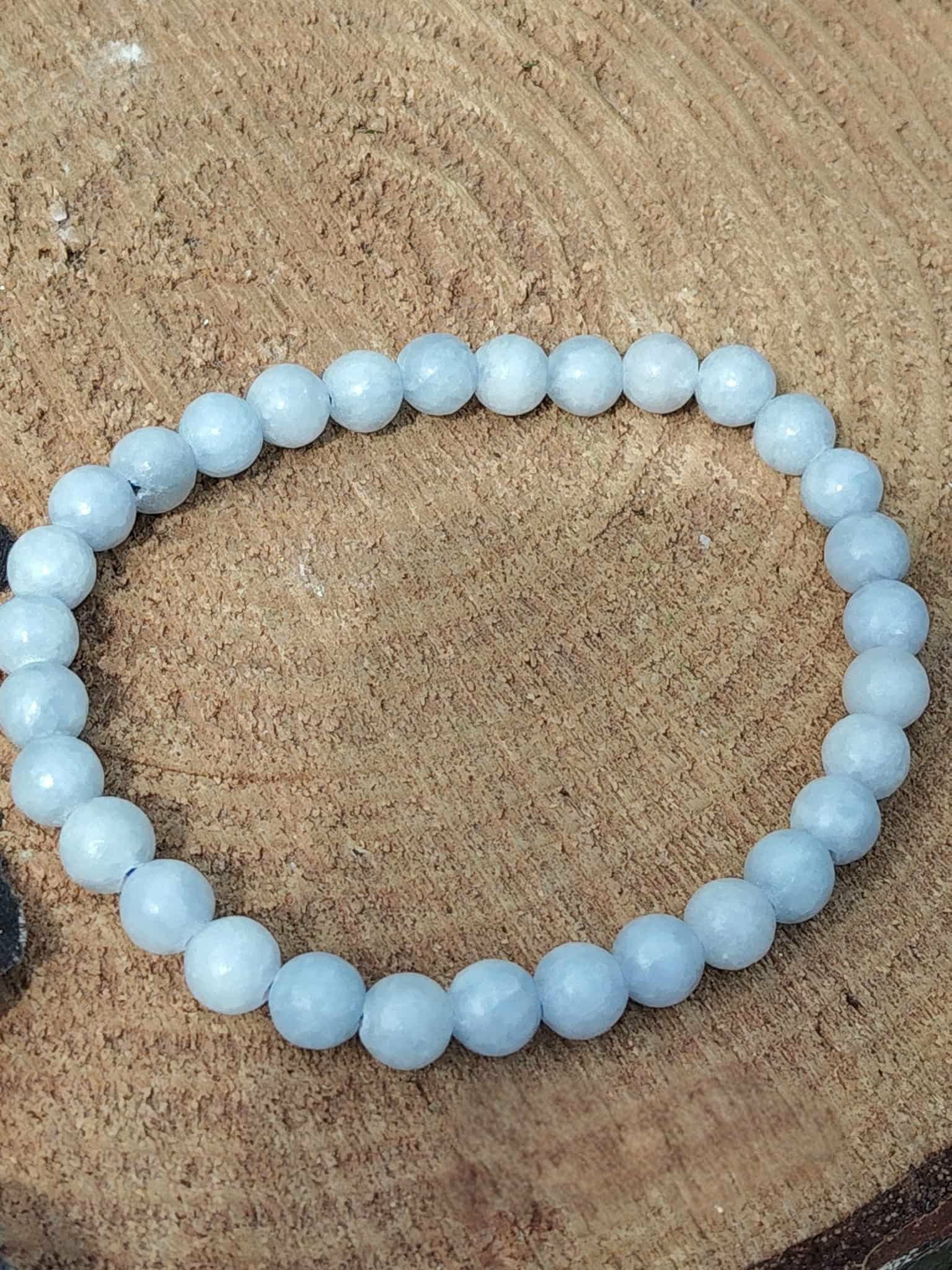 Bracelet célestite 6 mm photographié sur rondin de bois au fond naturel, perles bleu ciel nuancées, lâcher-prise, repos du mental et douceur relationnelle