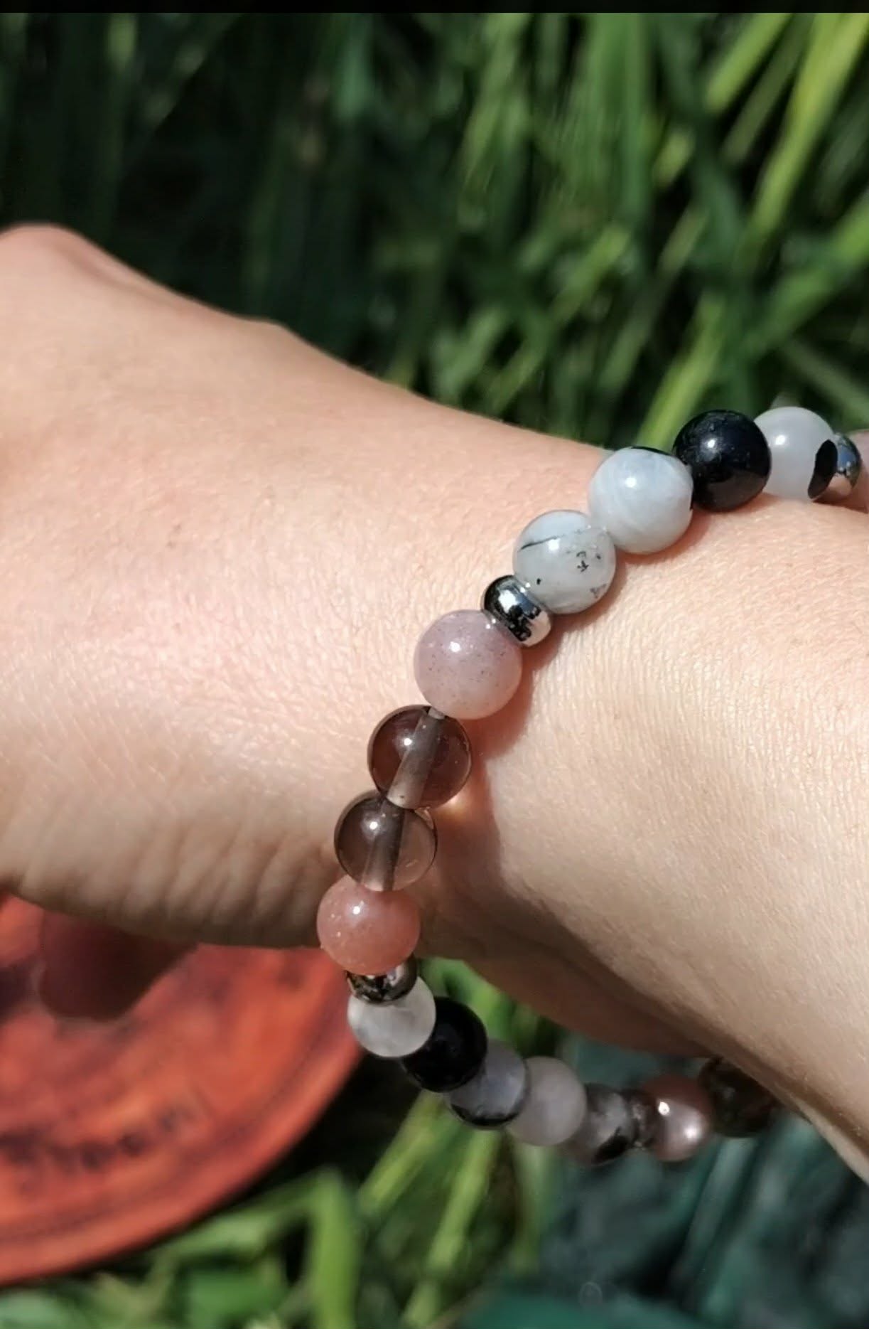 Bracelet Deuil porté au poignet sur fond de feuillage vert, soutien émotionnel, présence rassurante et apaisement du ressenti