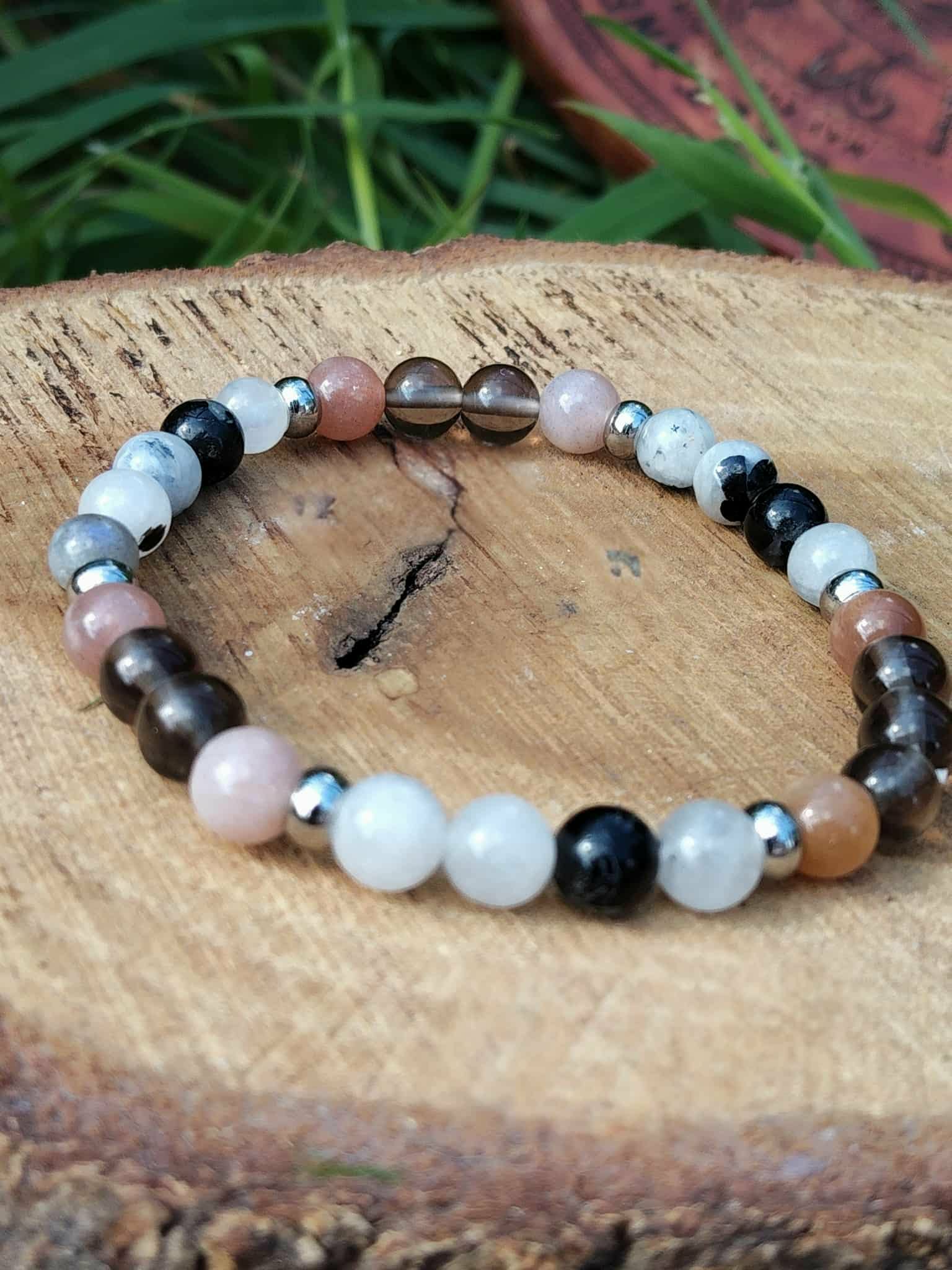 Bracelet Deuil 6 mm présenté sur plateau en bois avec feuillage vert, perles noires, blanches et rose pâle pour réconfort intérieur et stabilité émotionnelle