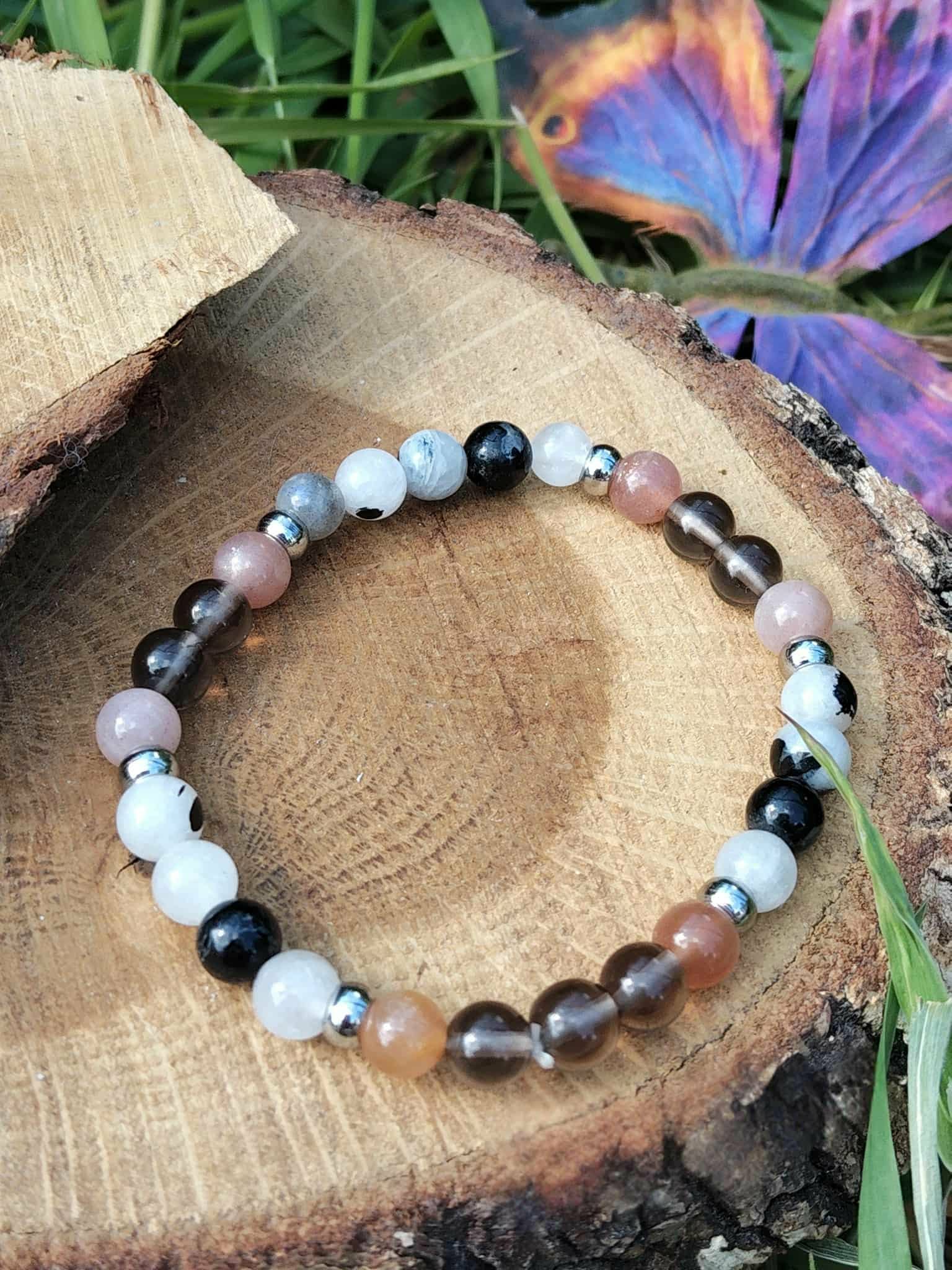 Bracelet Deuil sur rondin de bois avec feuillage et fleur en arrière-plan, ancrage doux, réconfort affectif et calme intérieur