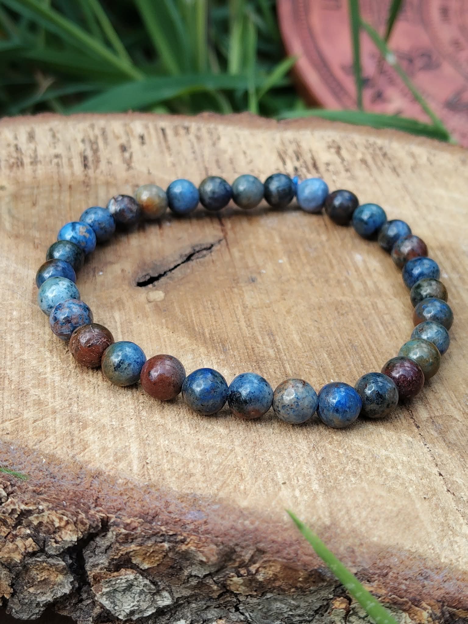 Bracelet dumortiérite en perles bleu denim et bleu profond sur support bois avec feuillage vert, discipline intérieure, focus et expression sereine