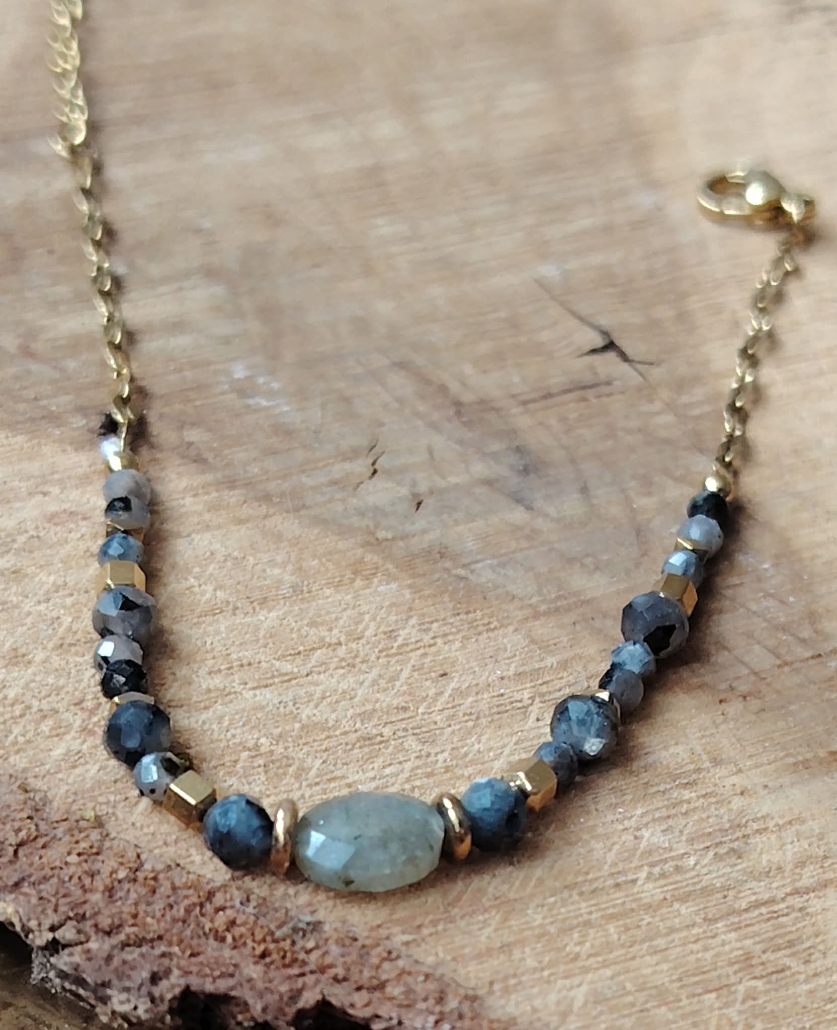 Bijou labradorite suspendu sur fond bois beige, bracelet acier inoxydable doré au style lumineux, stabilité émotionnelle et recul