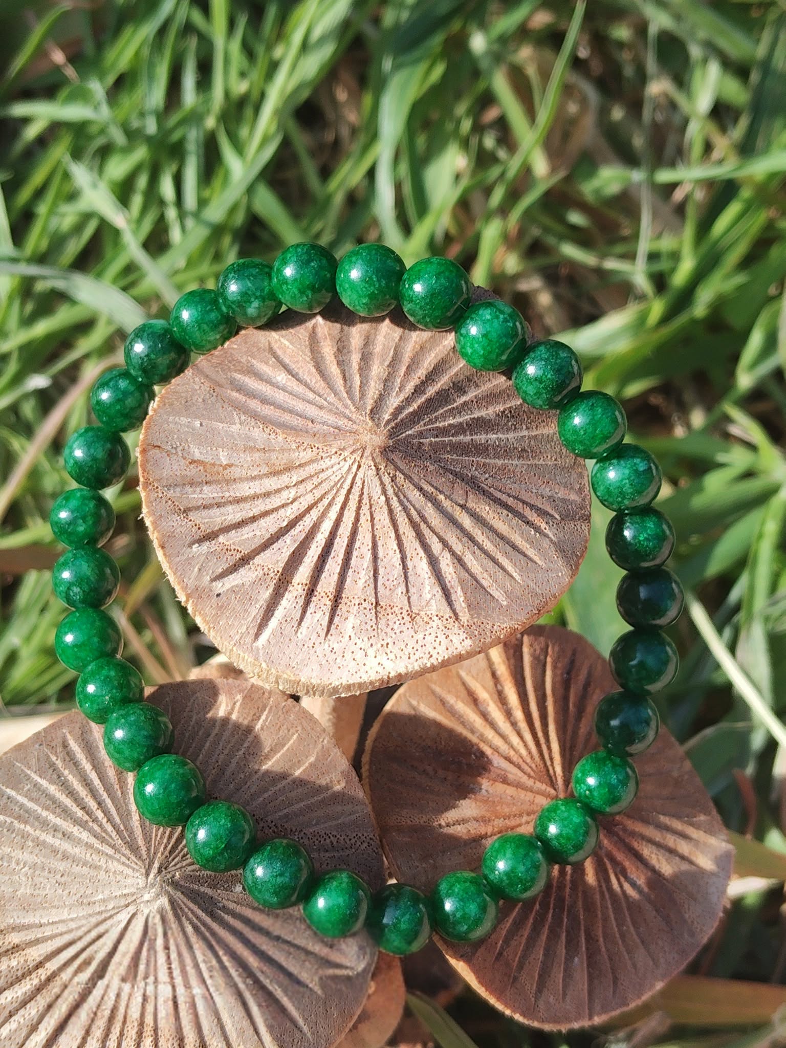 Bracelet jade africain 6 mm sur champignons en bois dans l’herbe, perles vert profond et vert mousse pour sérénité et recentrage du mental