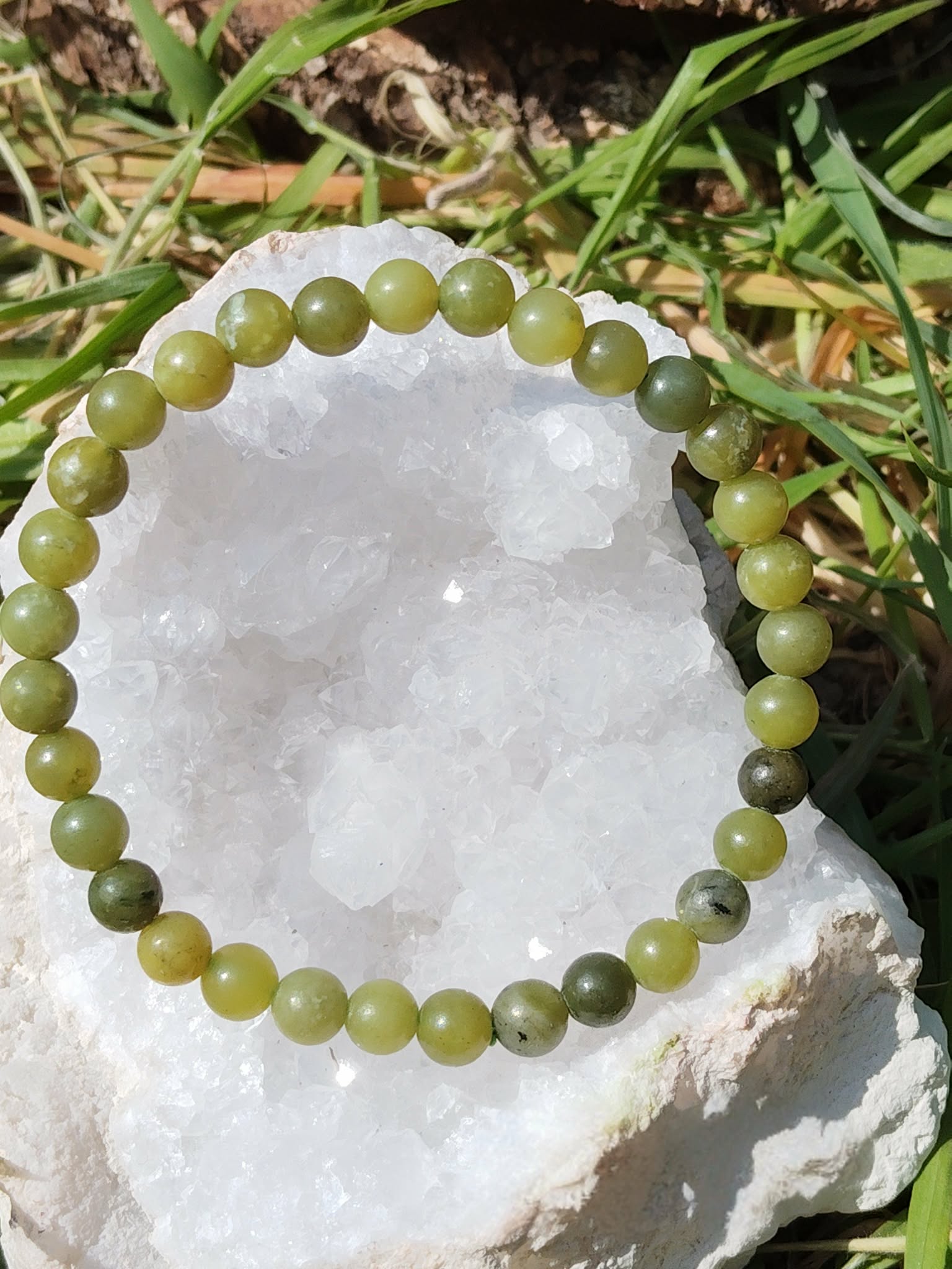 Bracelet jade du Canada 6 mm posé sur amas de quartz dans un décor nature, perles vert mousse, vert profond et nuances minérales, clarté douce, confiance et harmonie intérieure