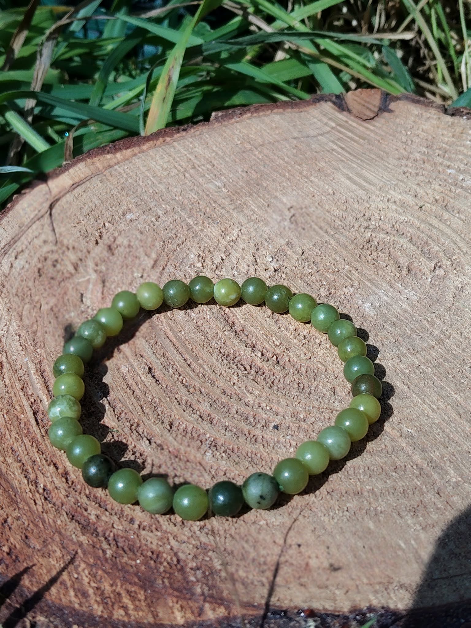Bracelet jade néphrite 6 mm sur rondin au fond boisé clair, perles vert olive, vert céladon et marbrures naturelles pour lâcher-prise et force calme