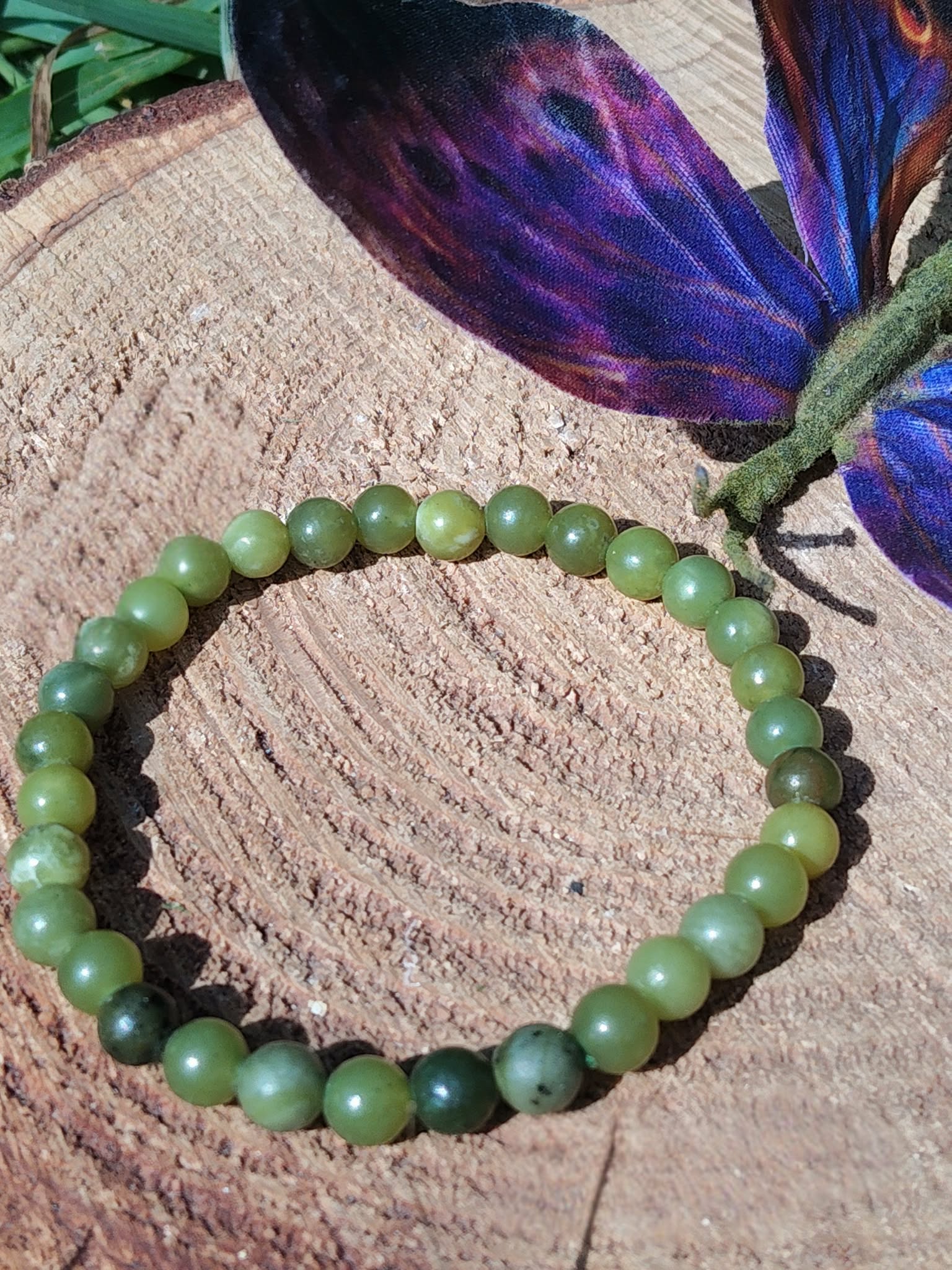 Bracelet jade du Canada 6 mm sur rondin de bois avec papillon bleu en arrière-plan, perles vert marbré et vert forêt pour ancrage léger et recentrage