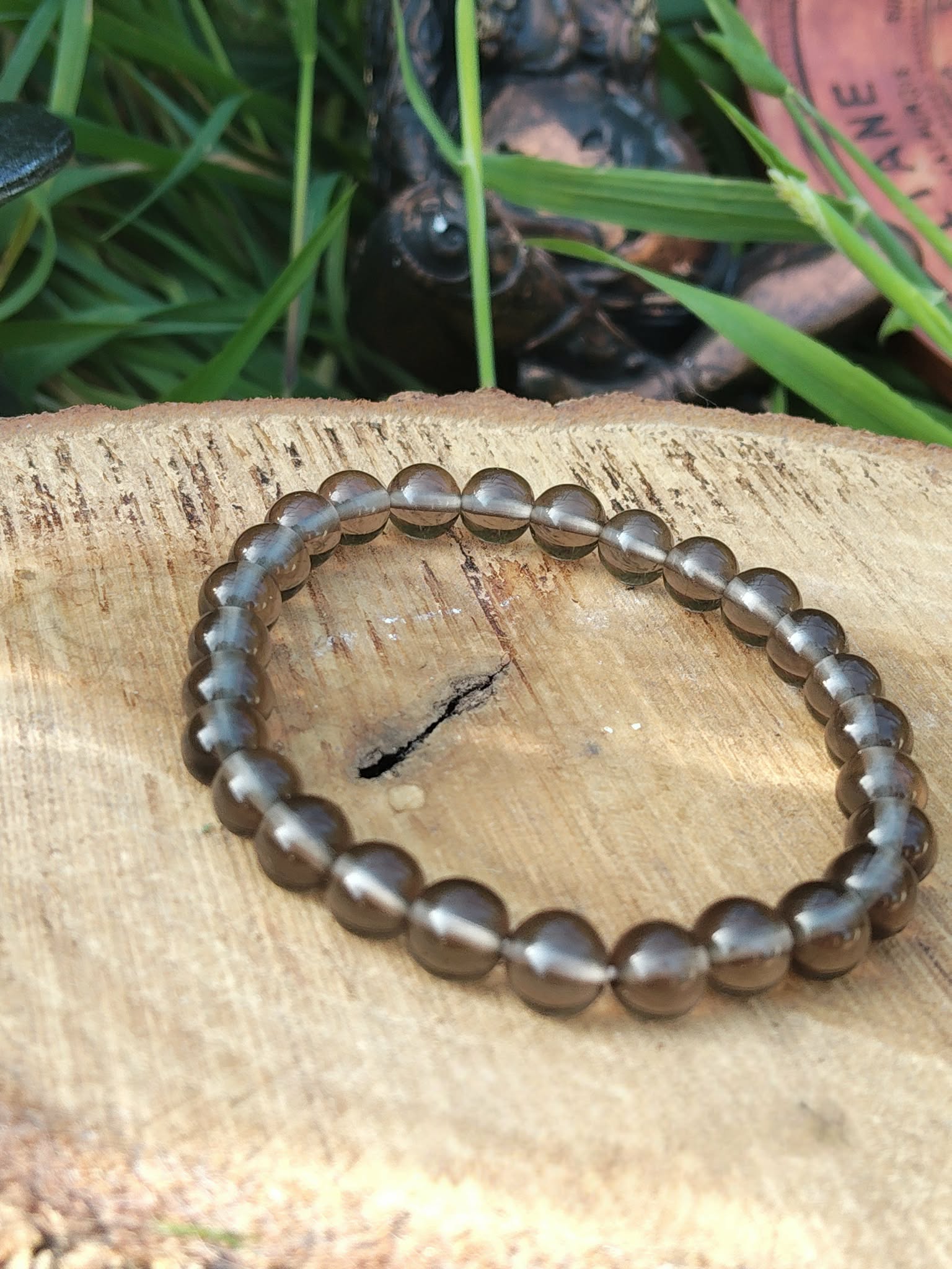 Bracelet obsidienne larme d’Apache 6 mm sur planche en bois clair avec feuillage vert, ancrage profond, réassurance émotionnelle et protection douce