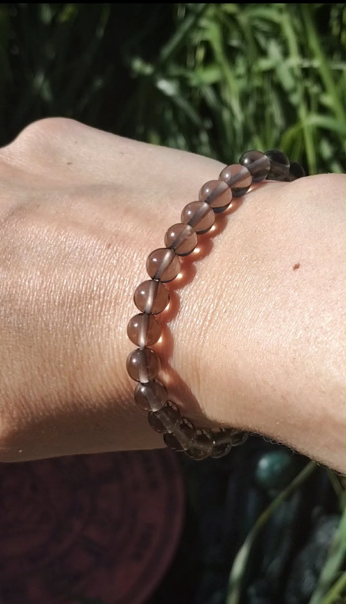 Bracelet obsidienne larme d’Apache 6 mm porté au poignet sur fond feuillage vert, présence calme, protection symbolique et équilibre émotionnel