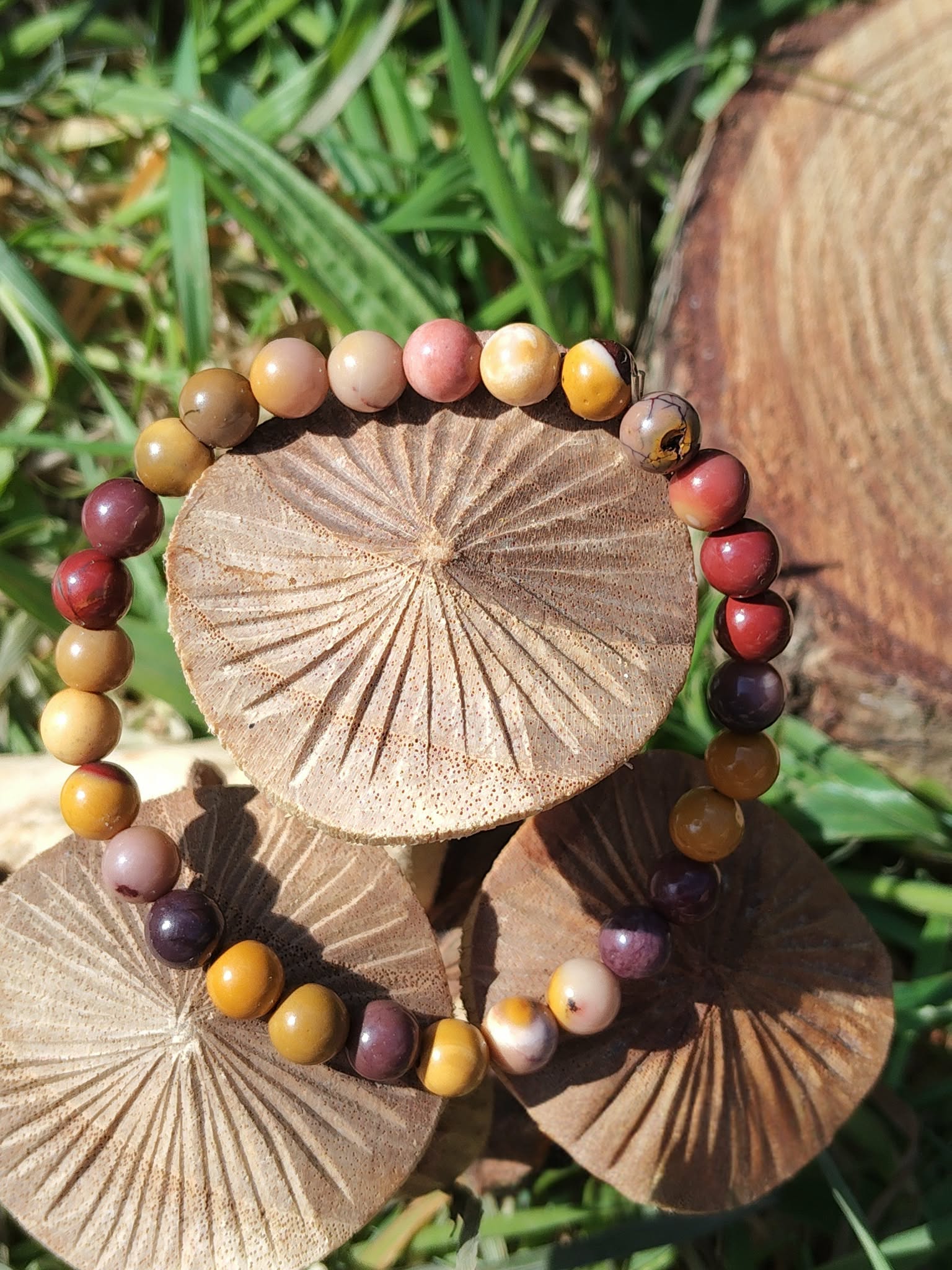Bracelet mookaïte 6 mm aux tons terreux jaune ocre, crème, bordeaux et prune sur rondelles de bois parmi le feuillage vert, courage, stabilité et passage à l’action