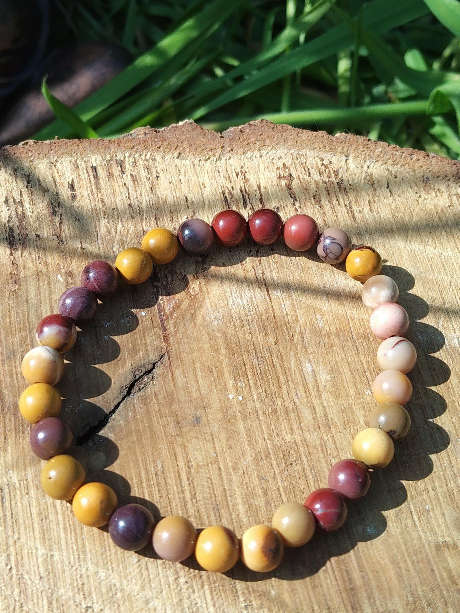 Bracelet mookaïte 6 mm aux tons terreux sur rondelles de bois parmi le feuillage vert, courage, passage à l’action et énergie d’enracinement