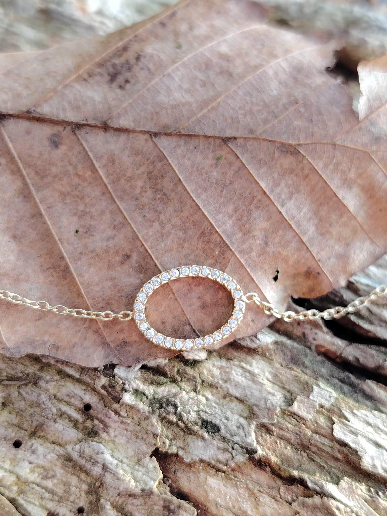 Bracelet fin acier inoxydable doré avec ovale pavé de strass sur bois clair et écorce, accessoire délicat au style lumineux.