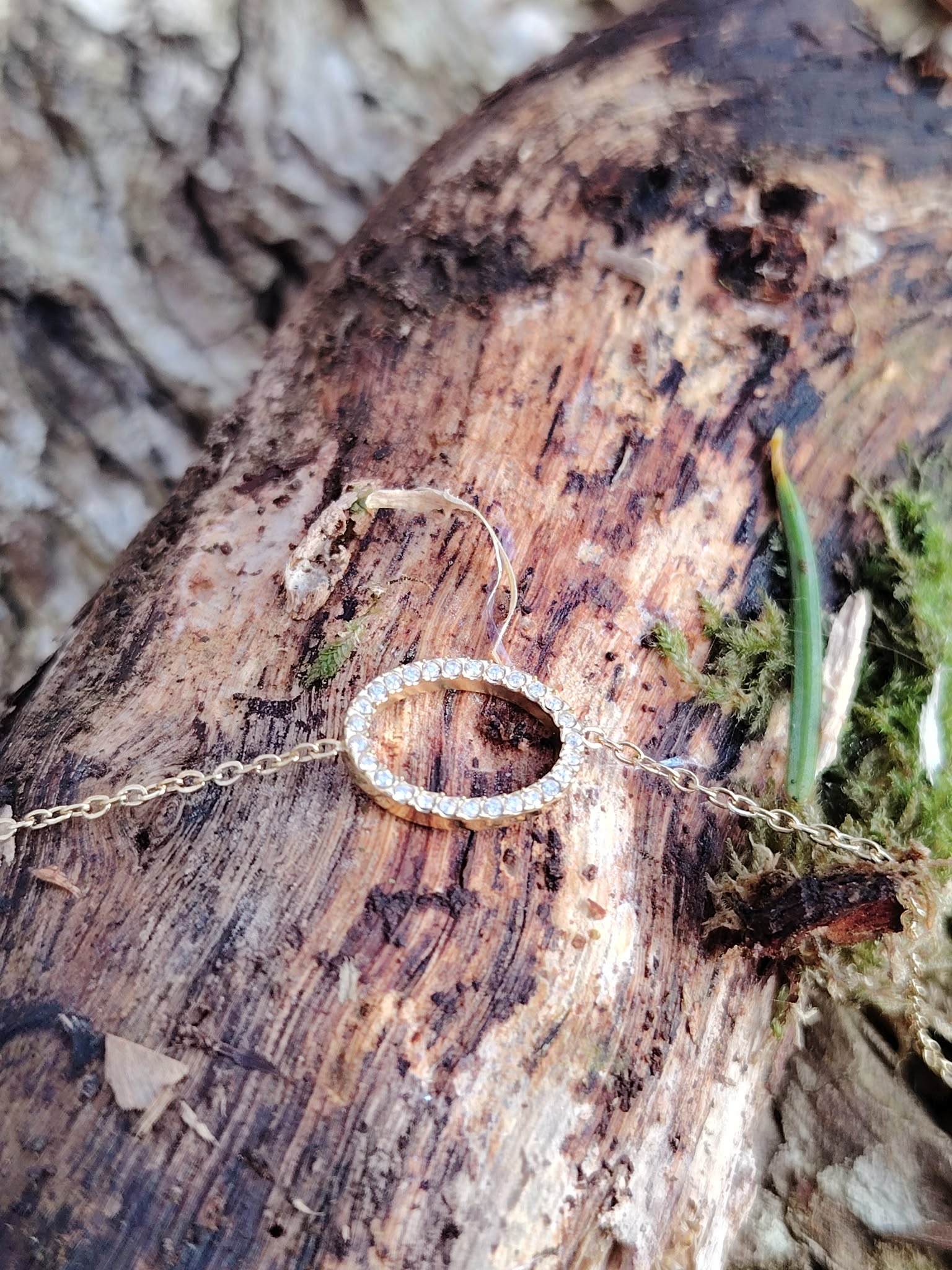 Bracelet doré en acier inoxydable avec ovale pavé de strass posé sur écorce, mousse et aiguilles de pin, style chic et raffiné