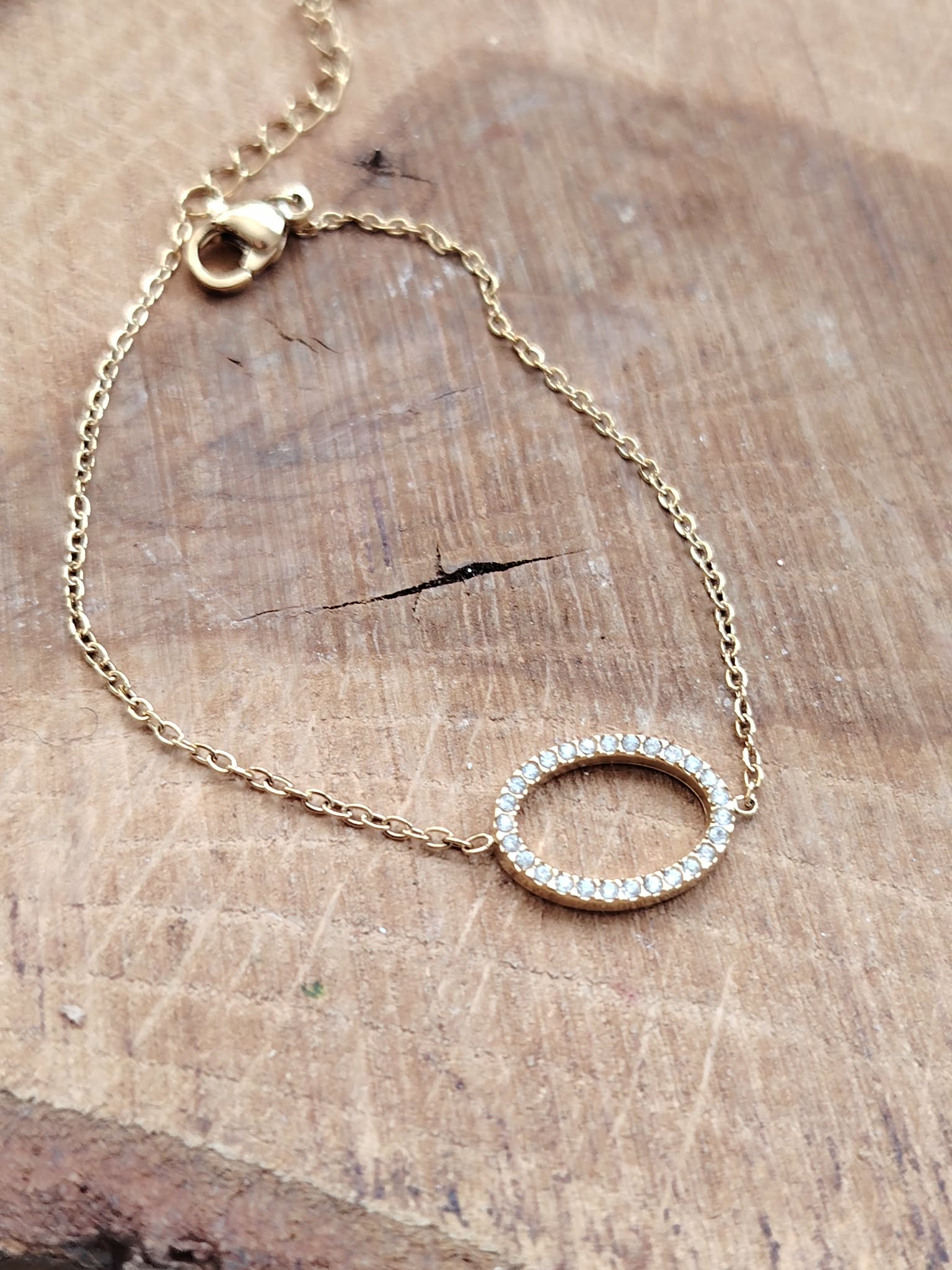 Bracelet doré acier inoxydable présenté à plat sur bois clair, chaîne fine et fermoir visibles, bijou élégant avec strass