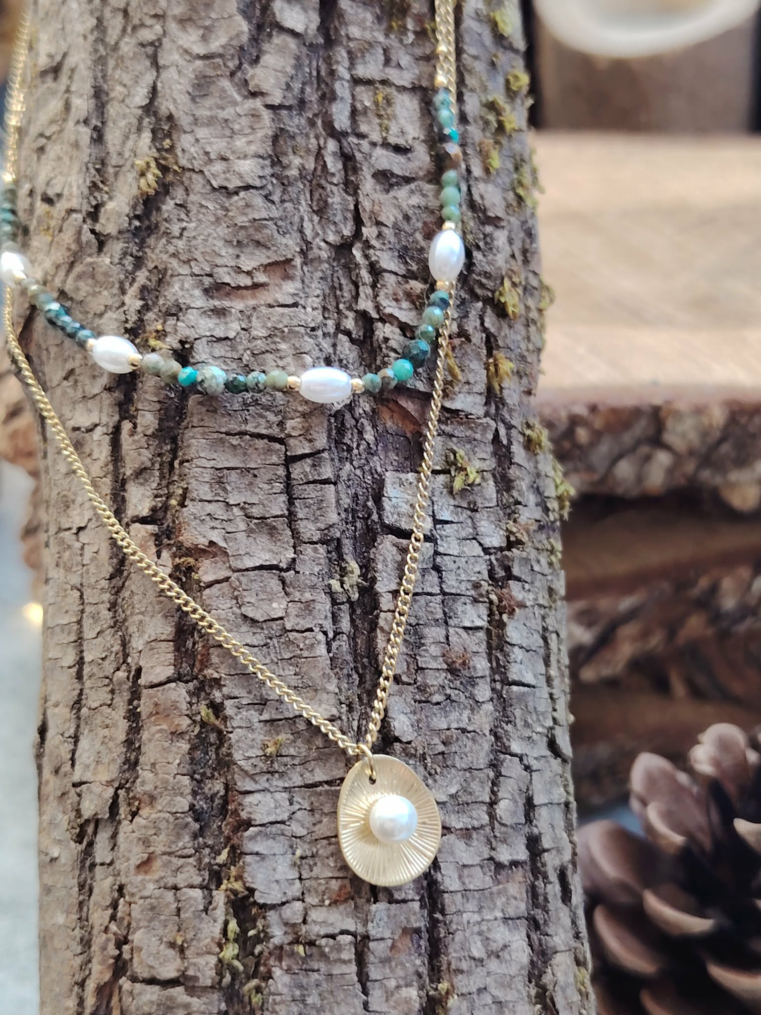 Collier double chaîne dorée acier inoxydable, perles blanches, pierres vertes, médaillon nacré, suspendu sur écorce.