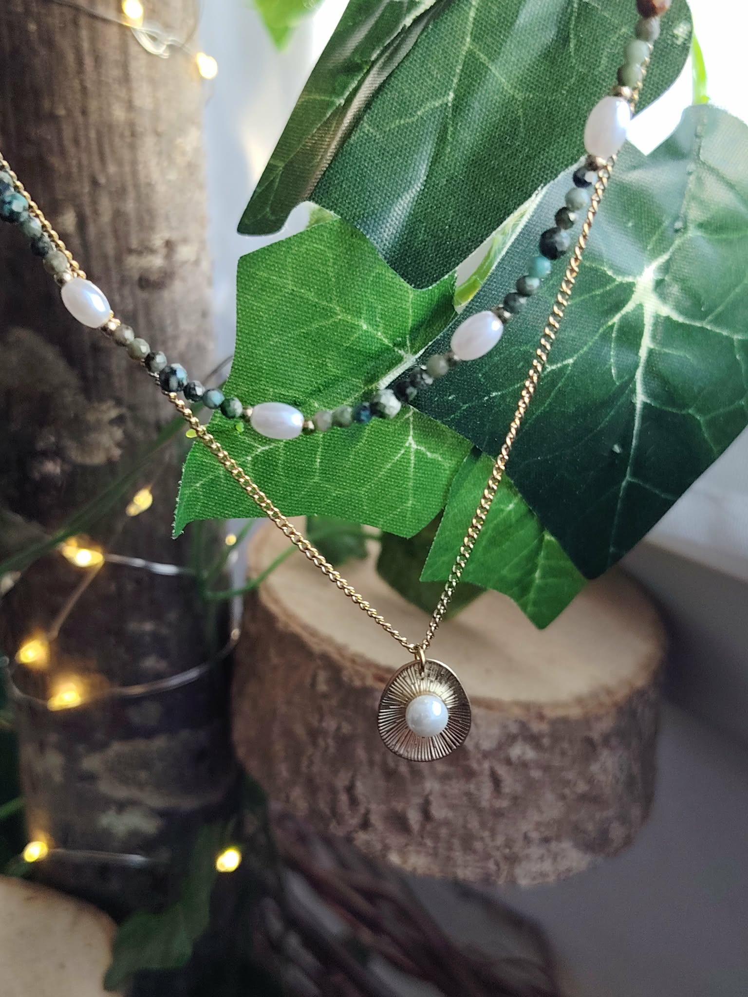 Collier double chaîne dorée acier inoxydable, perles blanches, pierres vertes, médaillon nacré, sur bois et feuilles vertes