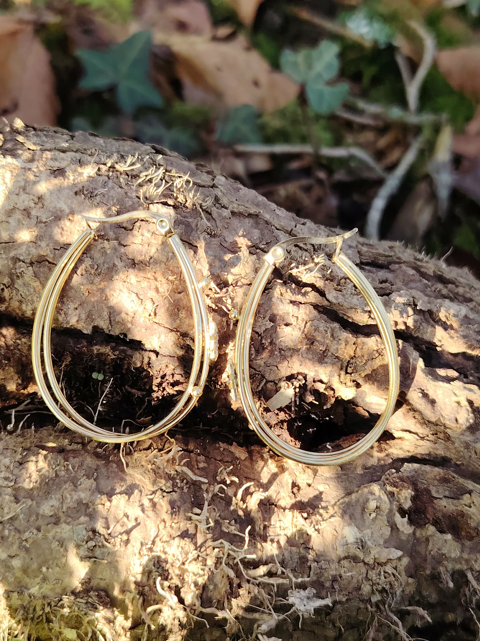 Boucles d’oreilles dorées 4 anneaux ovales reliés, détail étoile strassée, posées sur une écorce en décor nature avec feuilles et mousse en arrière-plan.