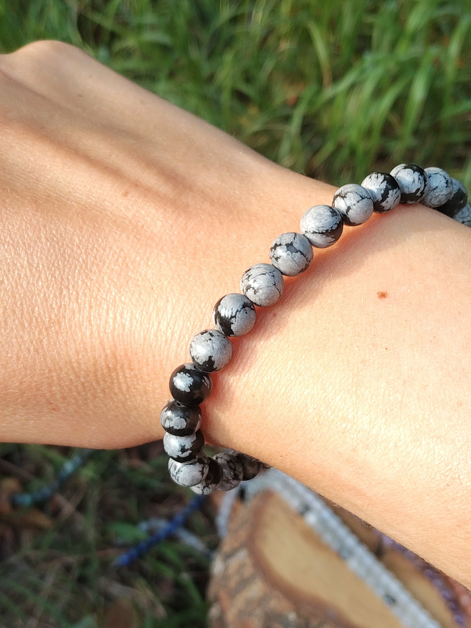 Bracelet obsidienne neige 6 mm porté au poignet, perles noir profond et gris moucheté, photo en extérieur avec feuillage, stabilité, protection, clarté mentale, recentrage.