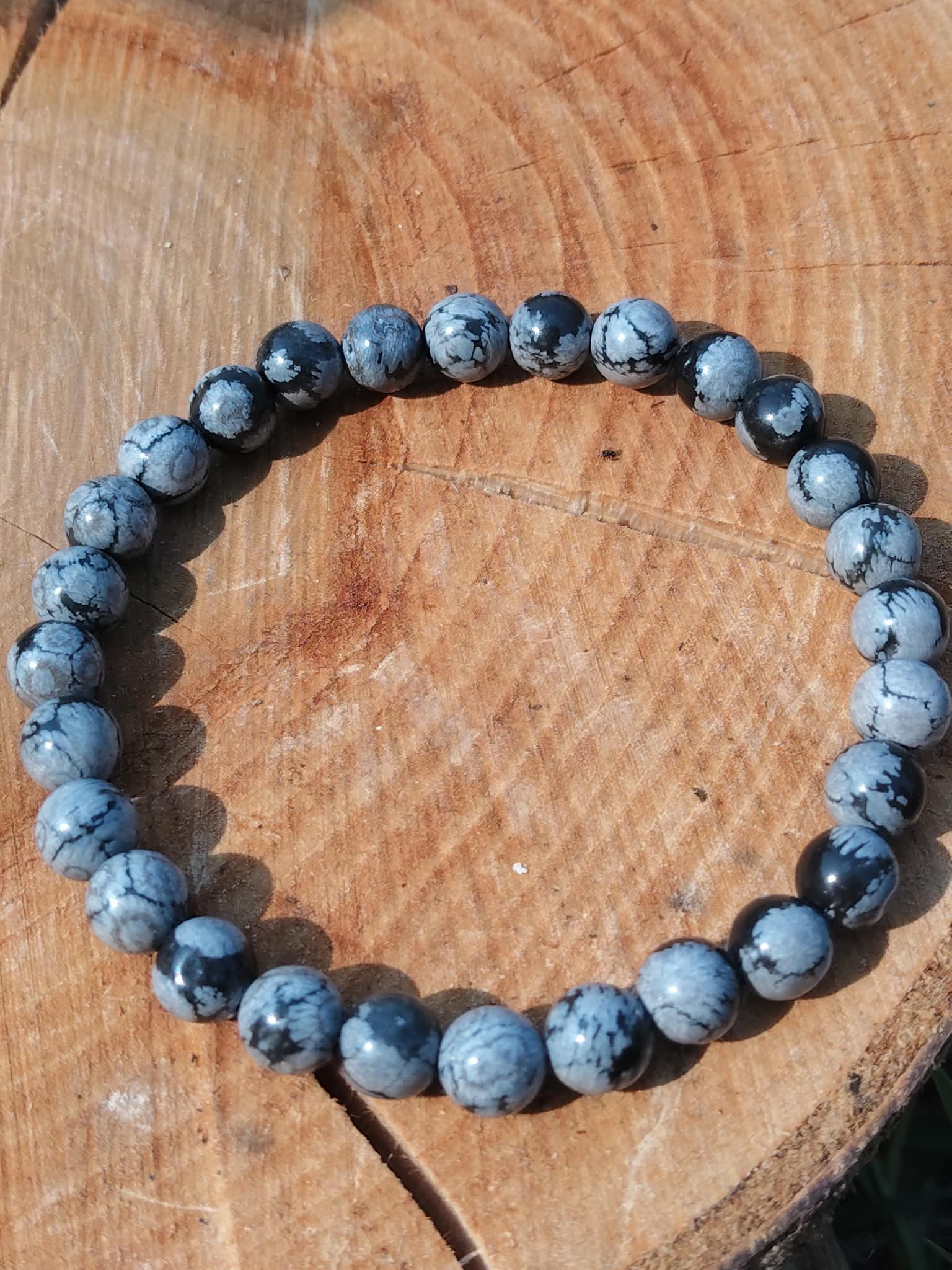 Bracelet obsidienne neige 6 mm sur planche en bois, perles noires et grises marbrées pour lucidité, recentrage et sérénité intérieure