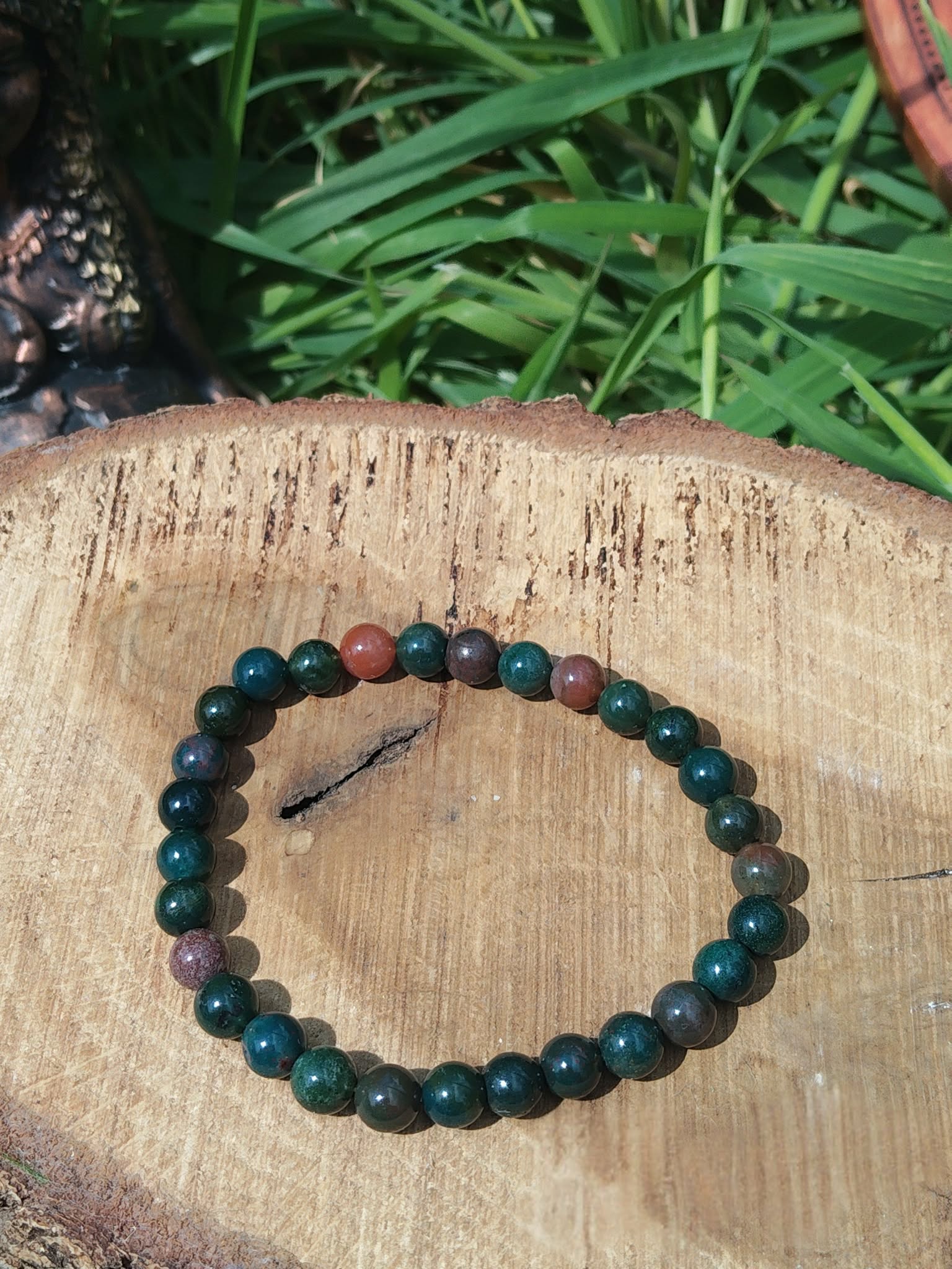 Bracelet jaspe héliotrope 6 mm sur rondin de bois, feuillage en fond ; ancrage, concentration, endurance.