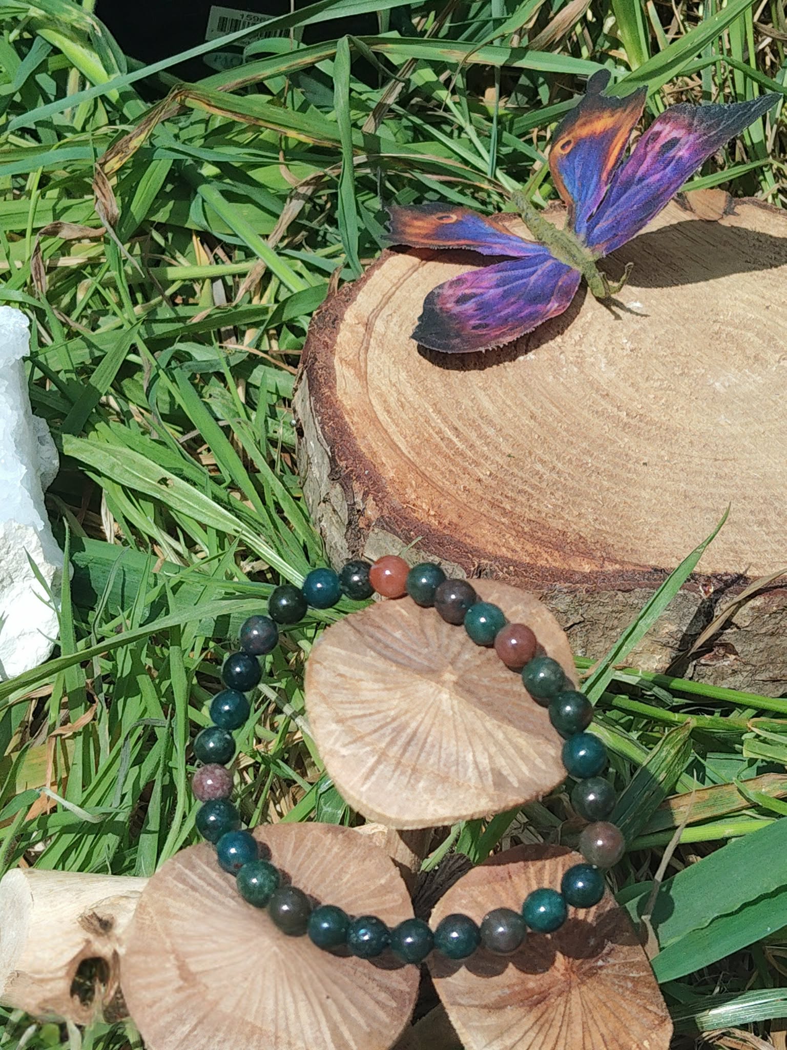 Bracelet jaspe héliotrope 6 mm sur rondin de bois, papillon violet et herbes autour ; énergie, détermination, recentrage.