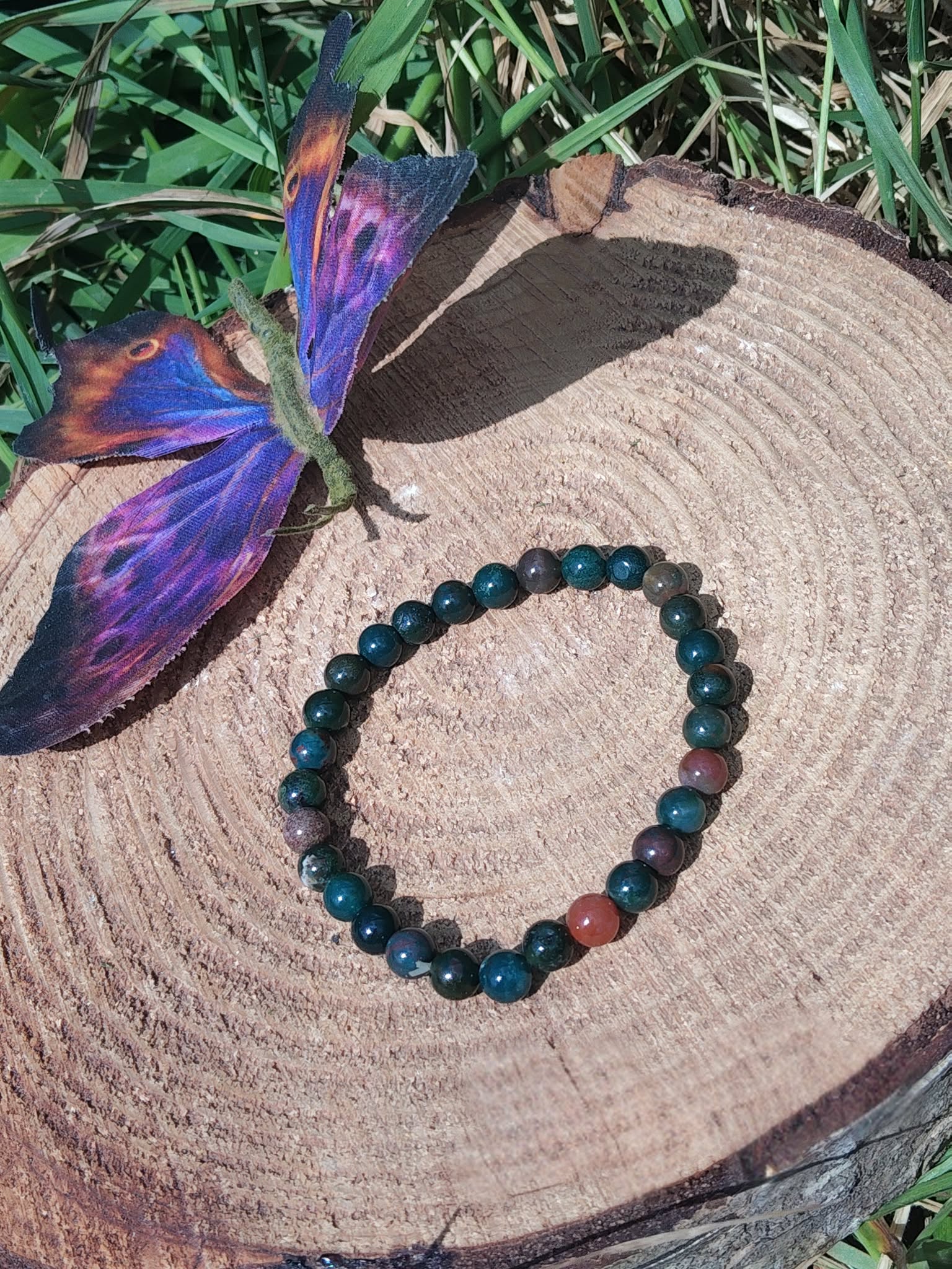 Bracelet jaspe héliotrope 6 mm sur rondin de bois, papillon bleu-violet et herbes ; force intérieure, vitalité, stabilité.