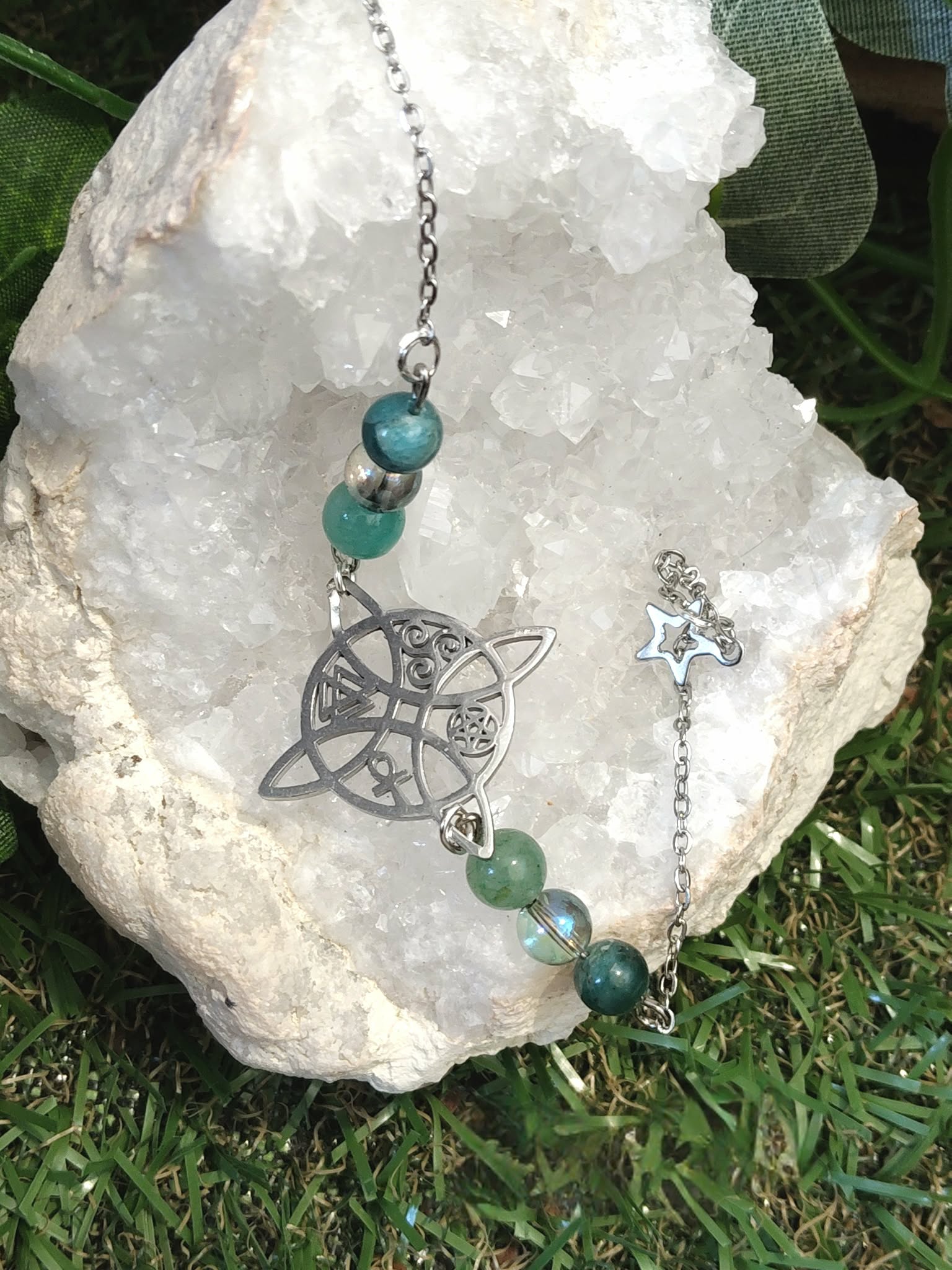 Bracelet symbole antique noir, amazonite et apatite bleu-vert avec Aqua Aura, présenté sur quartz brut et mousse, calme, communication, lucidité, stabilité émotionnelle.
