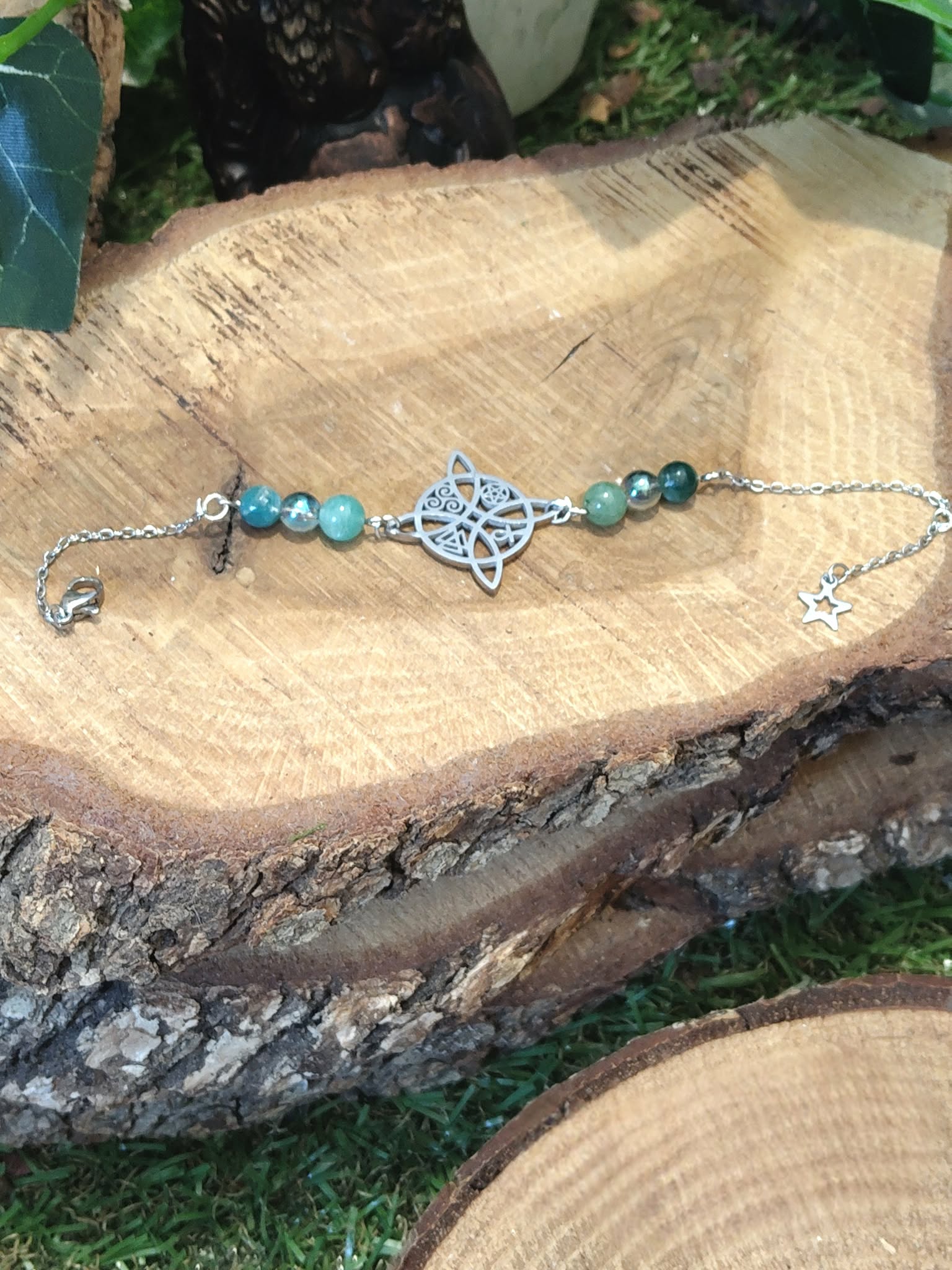 Bracelet symbole antique argenté, amazonite bleu-vert, Aqua Aura irisé, apatite turquoise, posé sur rondin de bois, ambiance nature, sérénité, expression, confiance, équilibre émotionnel