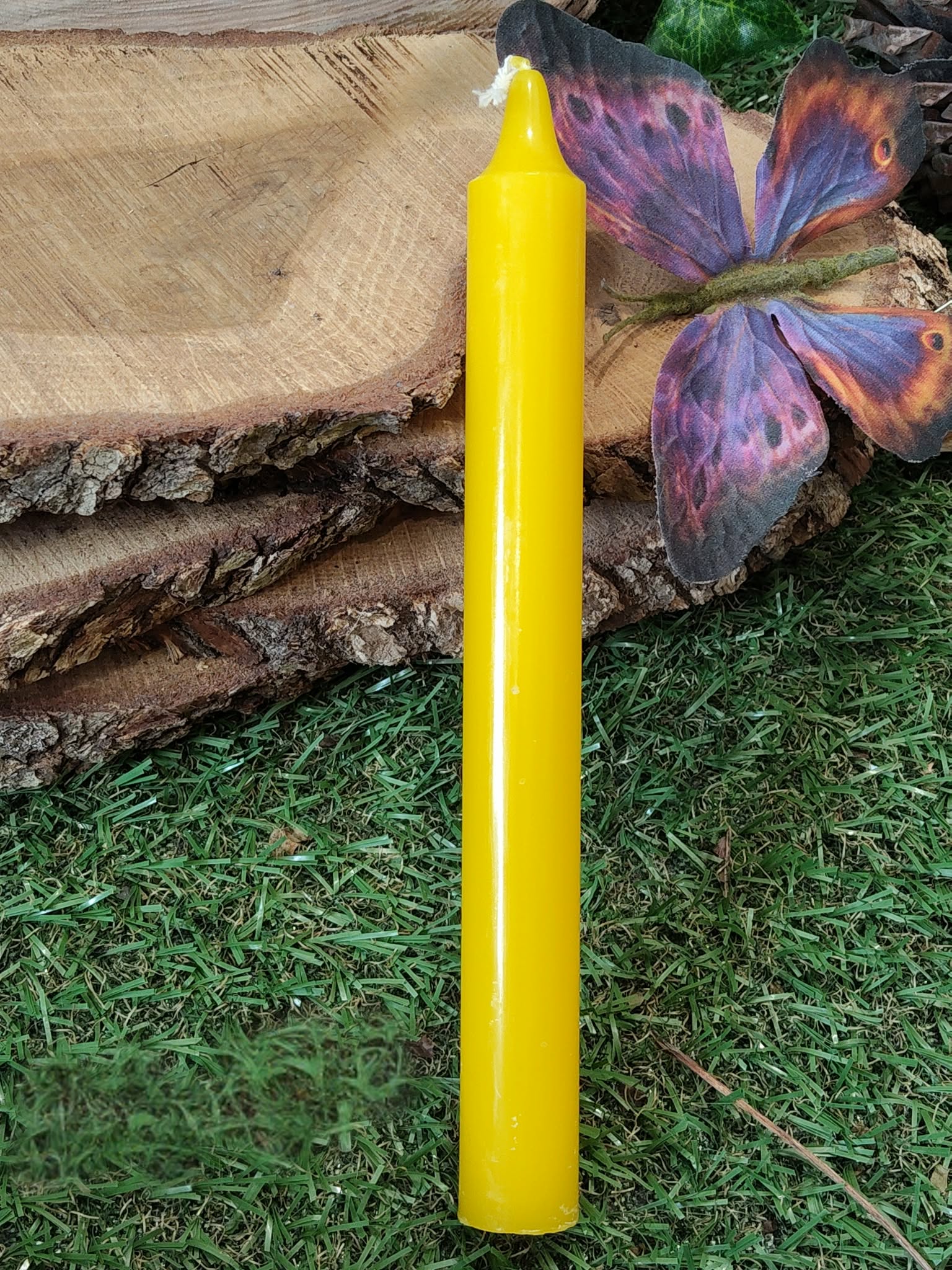 Bougie jaune devant rondin de bois, papillon violet-orange; joie, clarté, renouveau.
