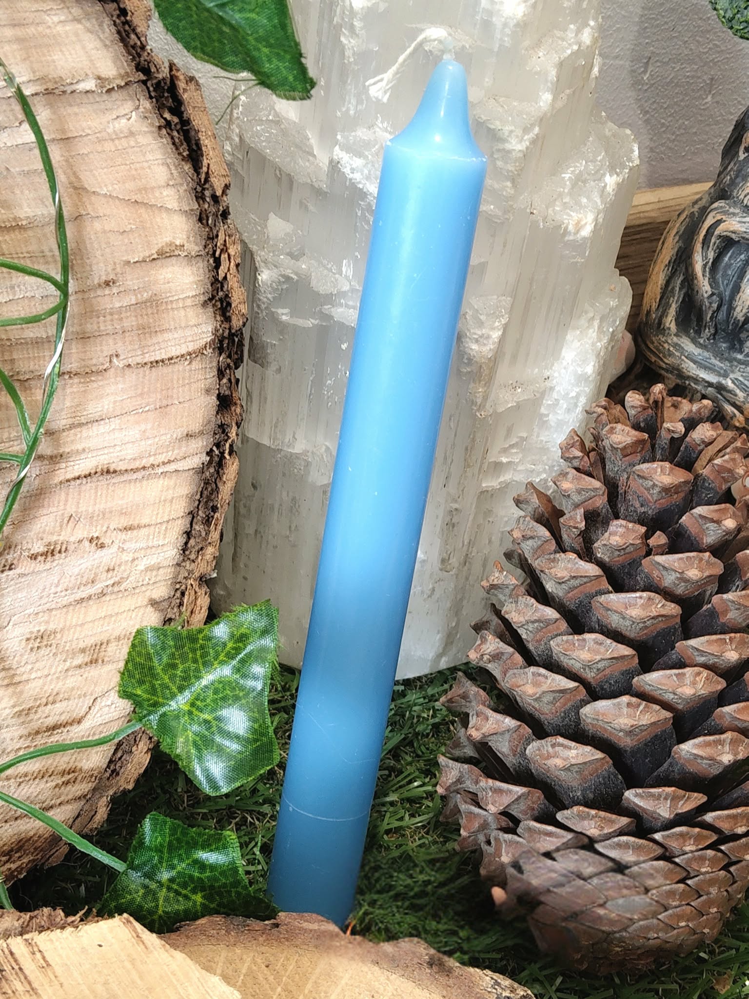 Bougie bleue fine dans un décor nature (bois, pomme de pin, lierre, mousse), apaise et aide à s’exprimer.