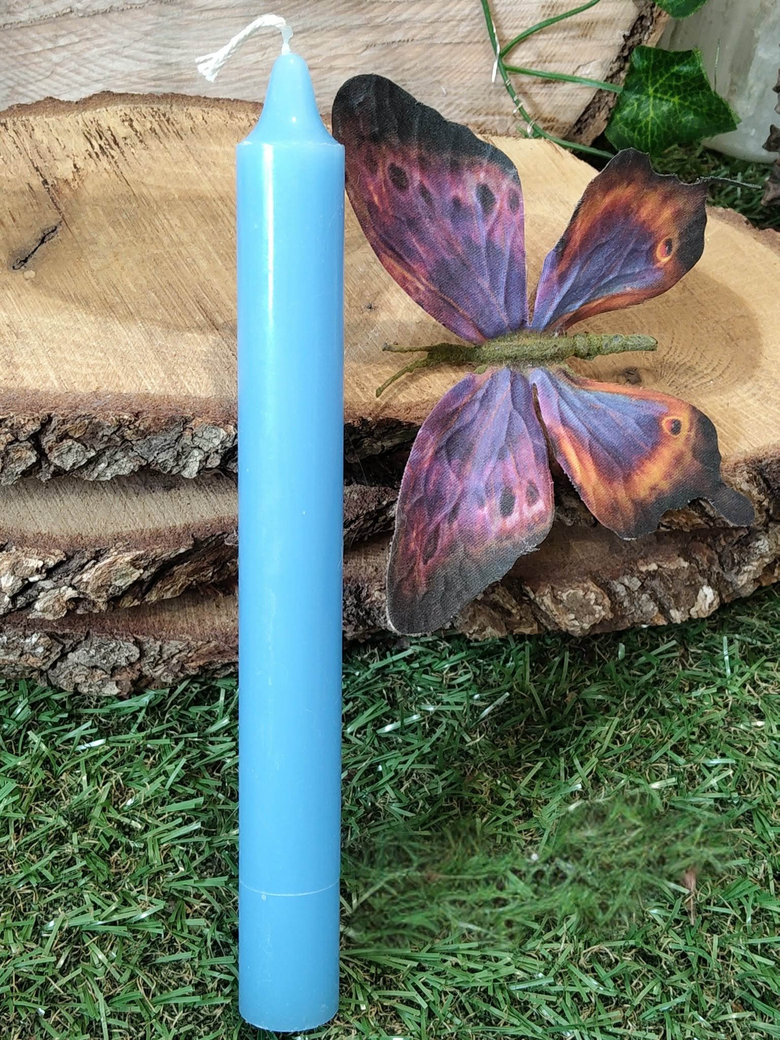 Bougie bleue sur mousse, rondins de bois et papillon violet-orange; calme, clarté, communication.