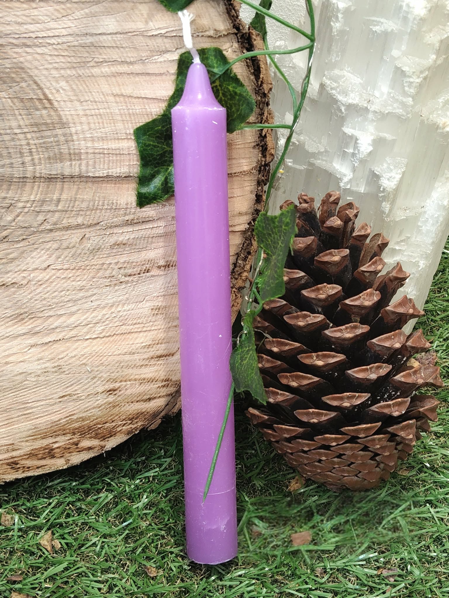 Bougie violette fine dans un décor nature (rondin de bois, pomme de pin, lierre, mousse), invite à l’intuition, au calme, au recentrage.