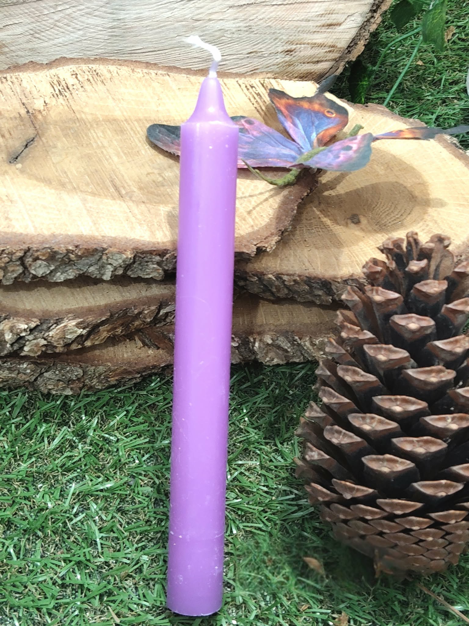 Bougie violette au centre, décor nature (mousse, rondins de bois, pomme de pin); calme intérieur, intuition, lâcher-prise.