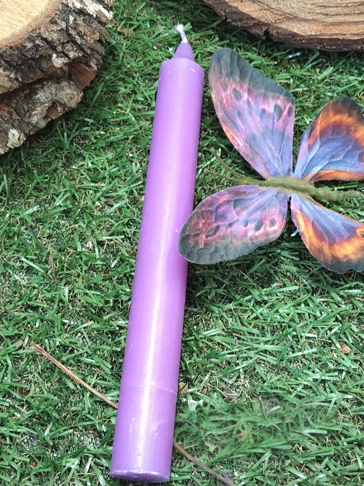 Bougie violette sur mousse, papillon violet-orange et pomme de pin floutée; intuition, calme, recentrage.