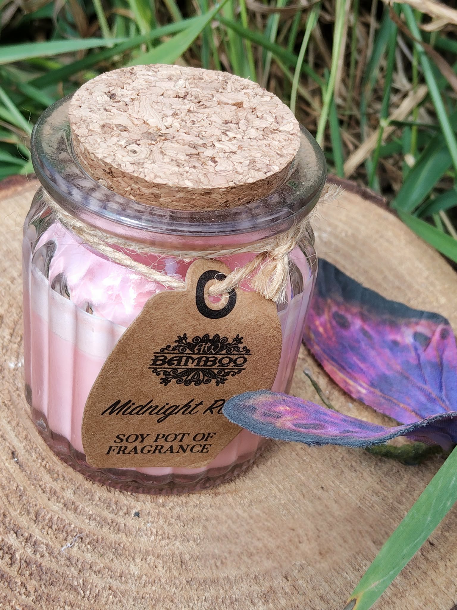 Bougie Rose de Minuit en cire de soja, pot verre couvercle liège, sur tranche de bois avec herbes et papillon décoratif, douceur, sérénité, harmonie.