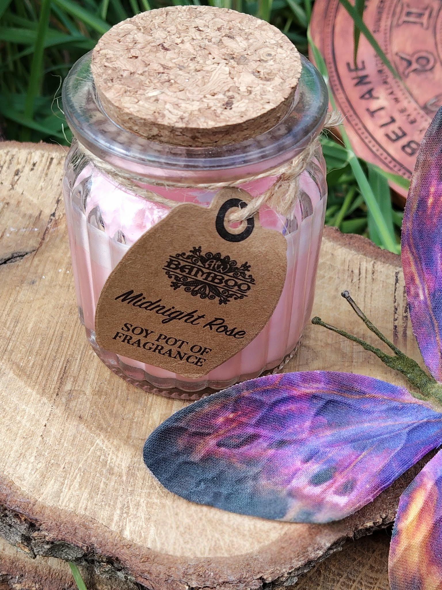 Bougie Rose de Minuit en cire de soja, pot verre couvercle liège, sur bois avec feuillage et papillon décoratif, douceur, romance, apaisement, harmonie.