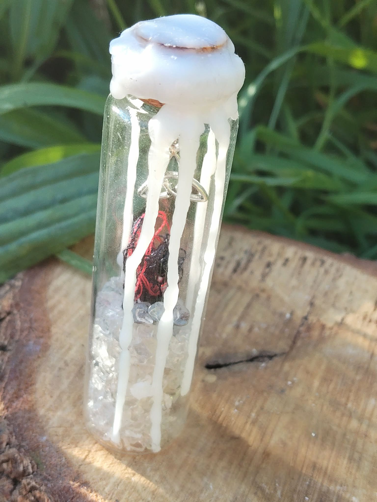 Spell jar en fiole de verre avec cire blanche et éclats de cristal de roche, photo en extérieur sur bois, ambiance protection et purification.