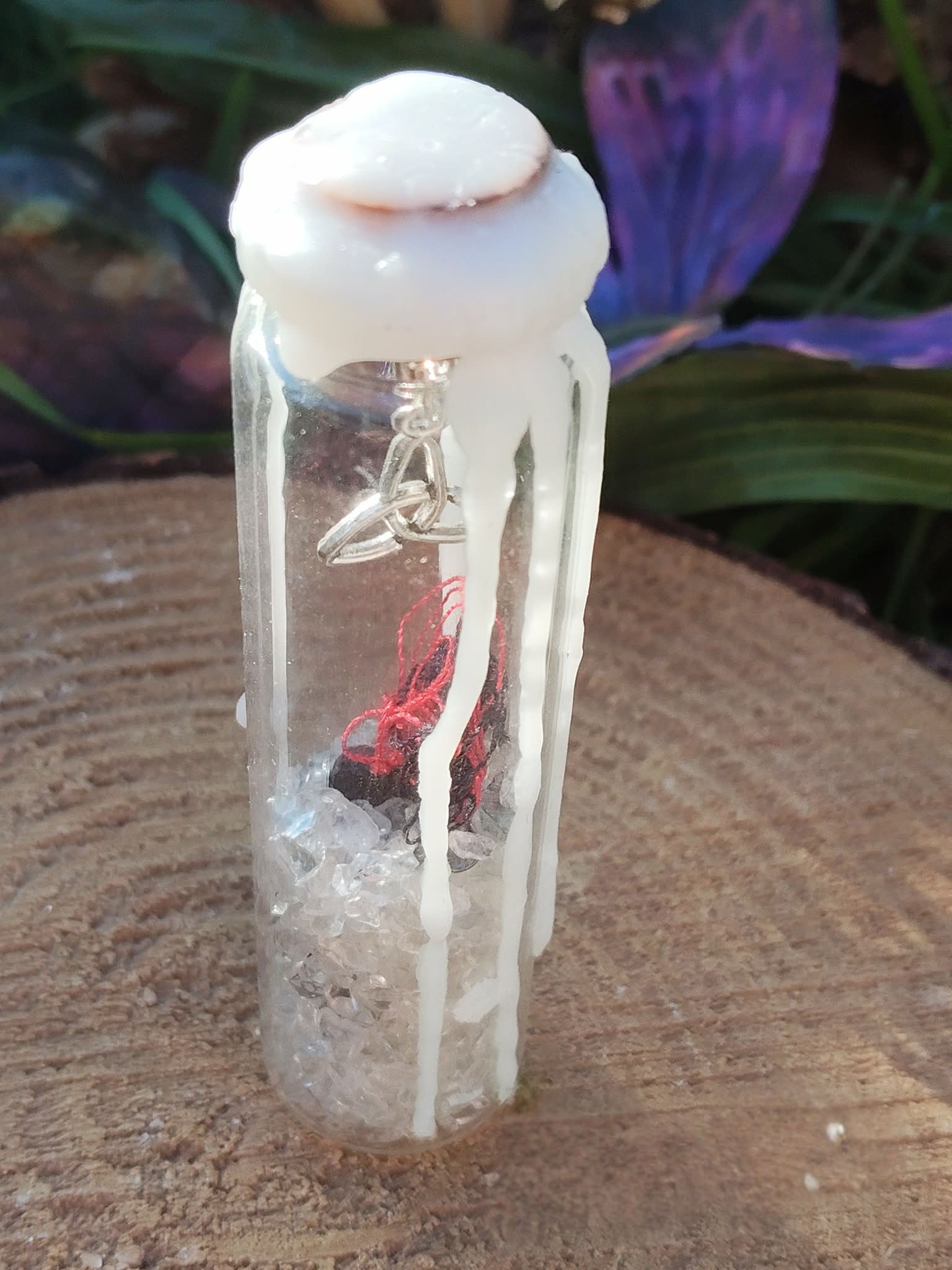 Spell jar en fiole de verre avec cristal de roche, fil rouge et cire blanche, posé sur bois avec décor sombre, ambiance protection et apaisement.