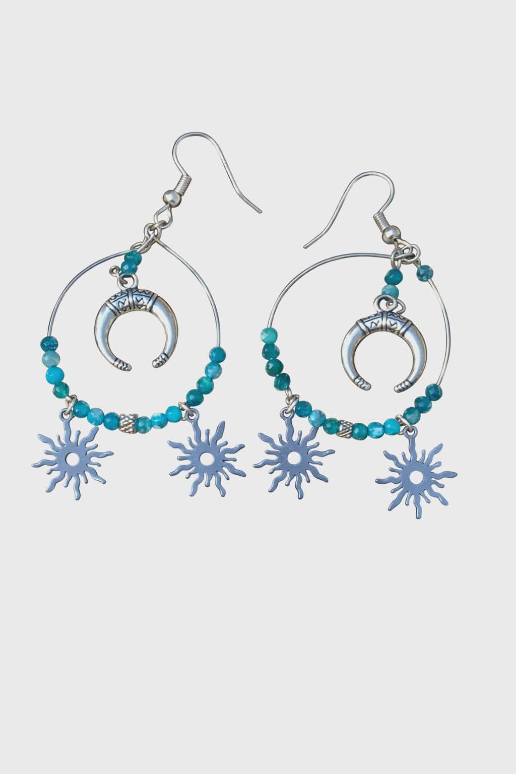 Boucles d’oreilles Atlante en apatite bleue création Magic Gaïa, perles facettées et charms lune/soleil argentés, posées sur rondin de bois au soleil dans l’herbe. Bienfaits : apaisement, expression, clarté intérieure, confiance douce