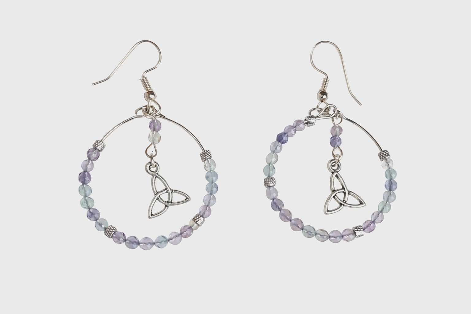 Boucles d’oreilles Hécate en fluorite facetté, création Magic Gaïa, perles facettées pastel et breloque triquetra argentée, photo sur fond blanc. Apaisement, clarté mentale, harmonie, recentrage