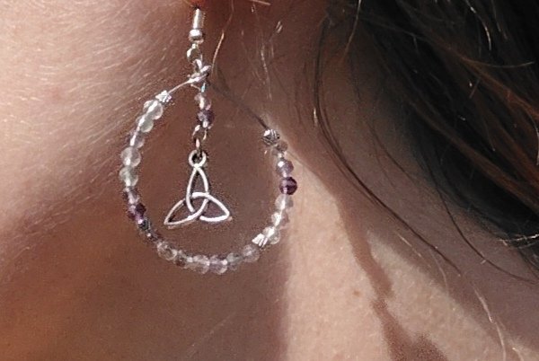 Boucle d’oreille Hécate en fluorite facettée, création Magic Gaïa, perles irisées dégradées et symbole triquetra argenté, photo portée à l’oreille en lumière douce. Calme, concentration, équilibre émotionnel, lucidité