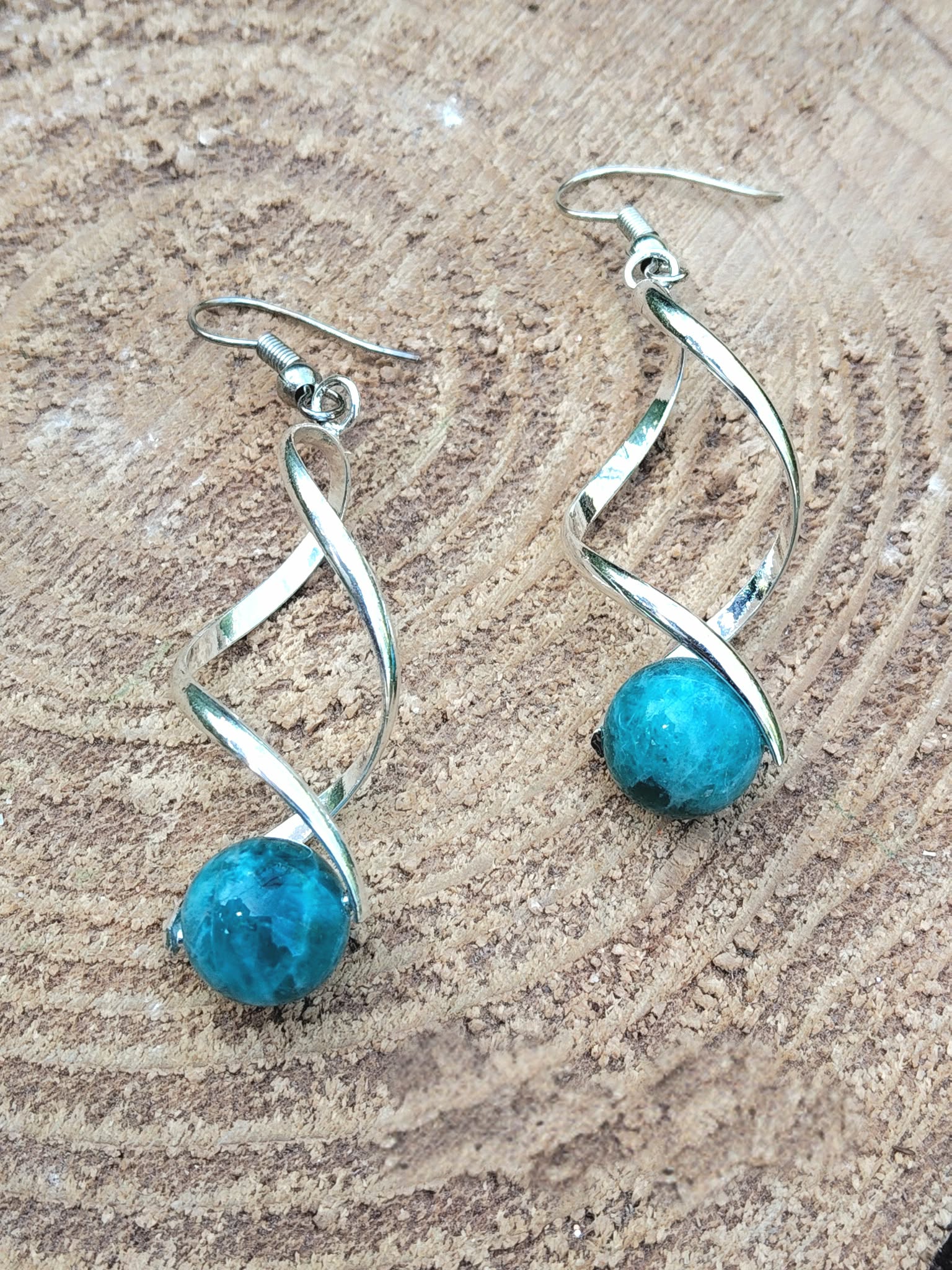 Boucles d’oreilles spirales argentées et perles d’apatite bleue sur bois clair, focus, inspiration, communication.